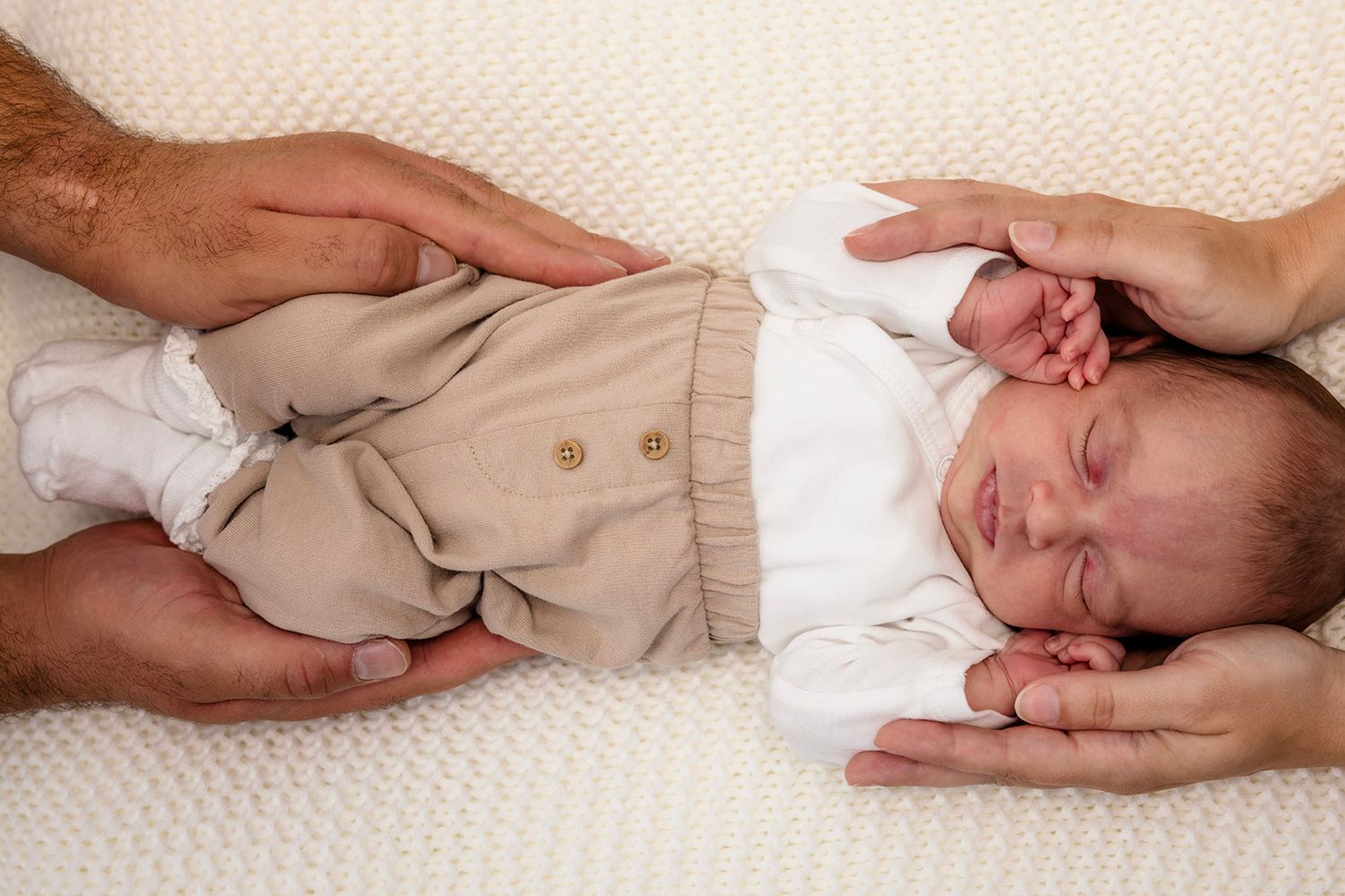 A series of connected newborn baby photos showing gentle hands cradling a sleeping infant in beige clothing.