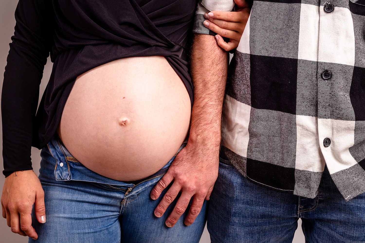 A row of people wearing casual clothing showing off their pregnant bellies in a group maternity photo.