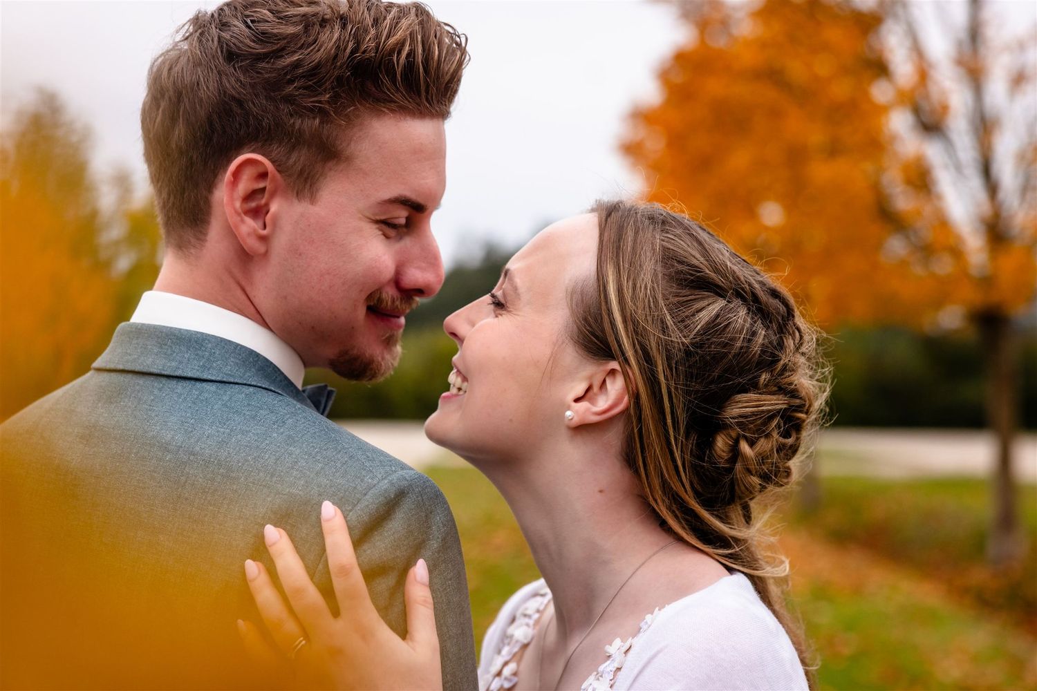A romantic autumn wedding portrait with a couple sharing an intimate moment against vibrant fall foliage.