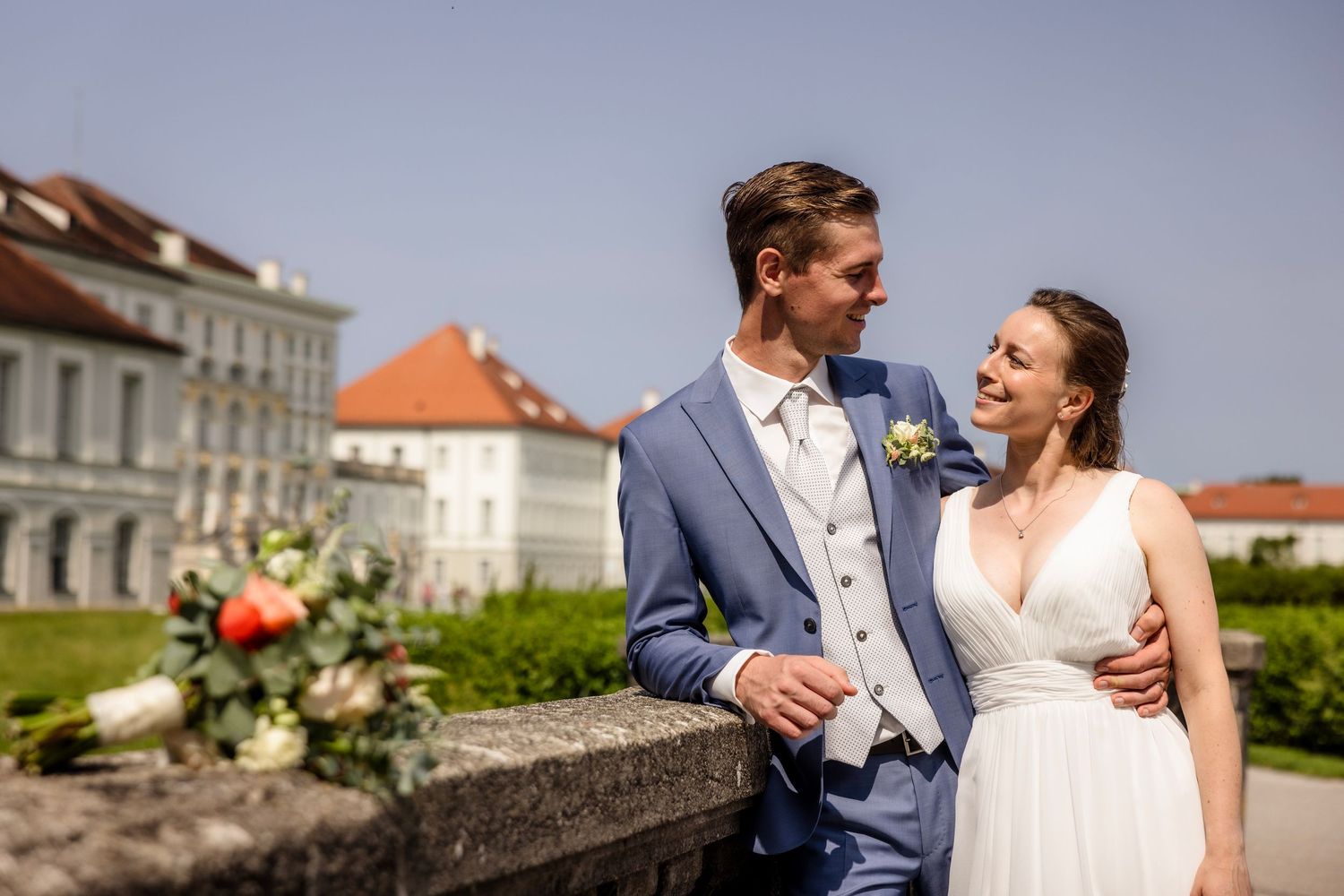 Bride and groom share a romantic moment outdoors near a grand palace on their wedding day.