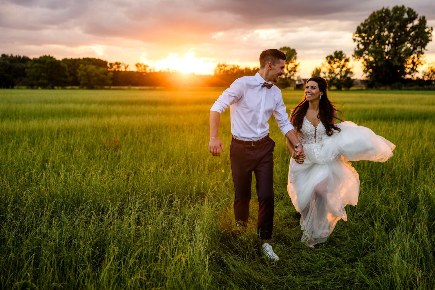 A couple shares a romantic moment in a sunlit meadow during golden hour as the sun sets behind them.