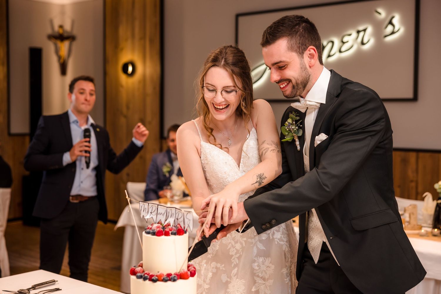 Bride and groom smiling while cutting their wedding cake together at an elegant restaurant reception venue.