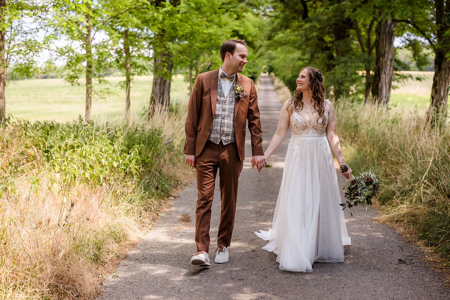 A couple walks together on a tree-lined path during a romantic outdoor photoshoot.