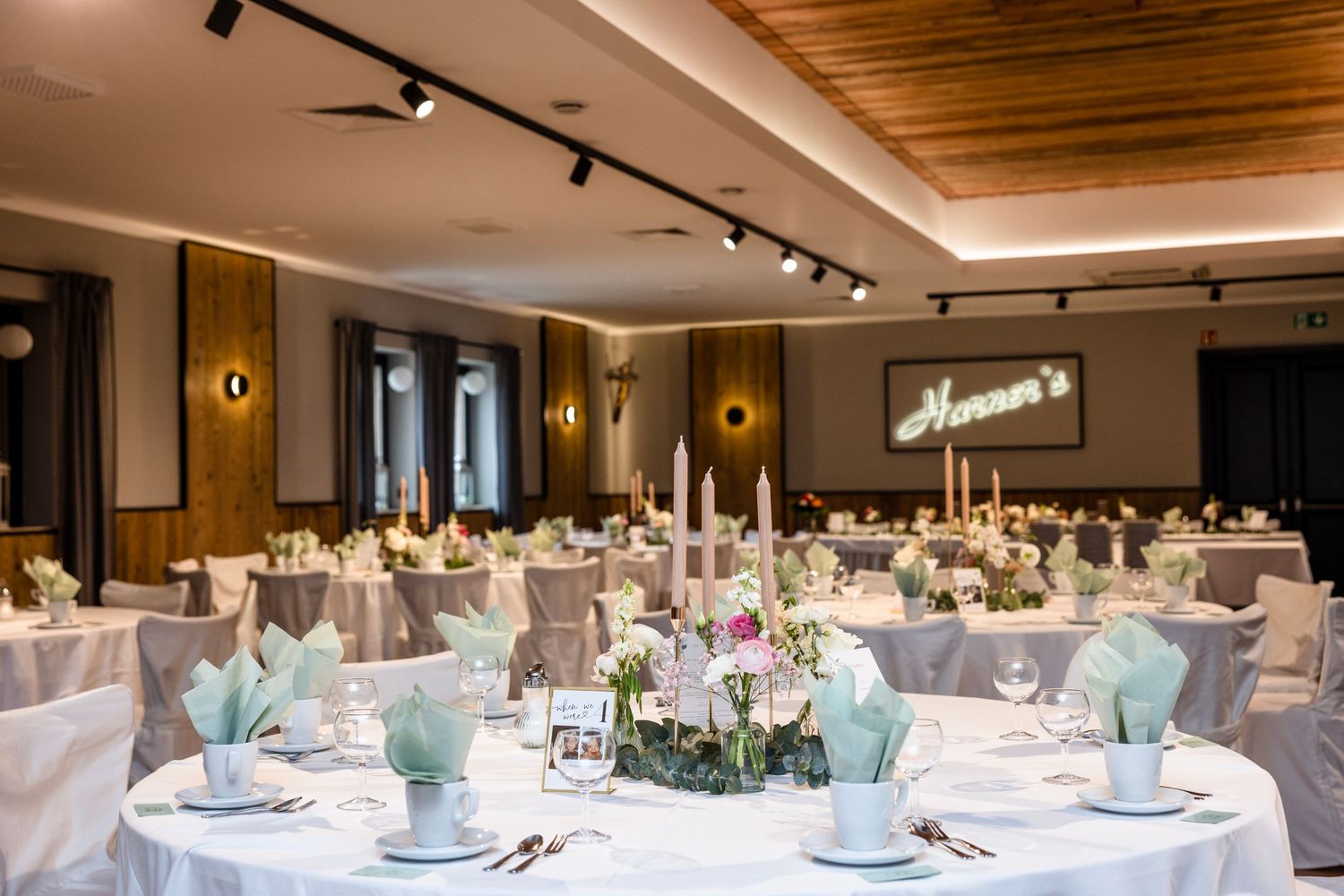 Elegant wedding reception venue with round tables decorated in mint and white linens, floral centerpieces and track lighting.