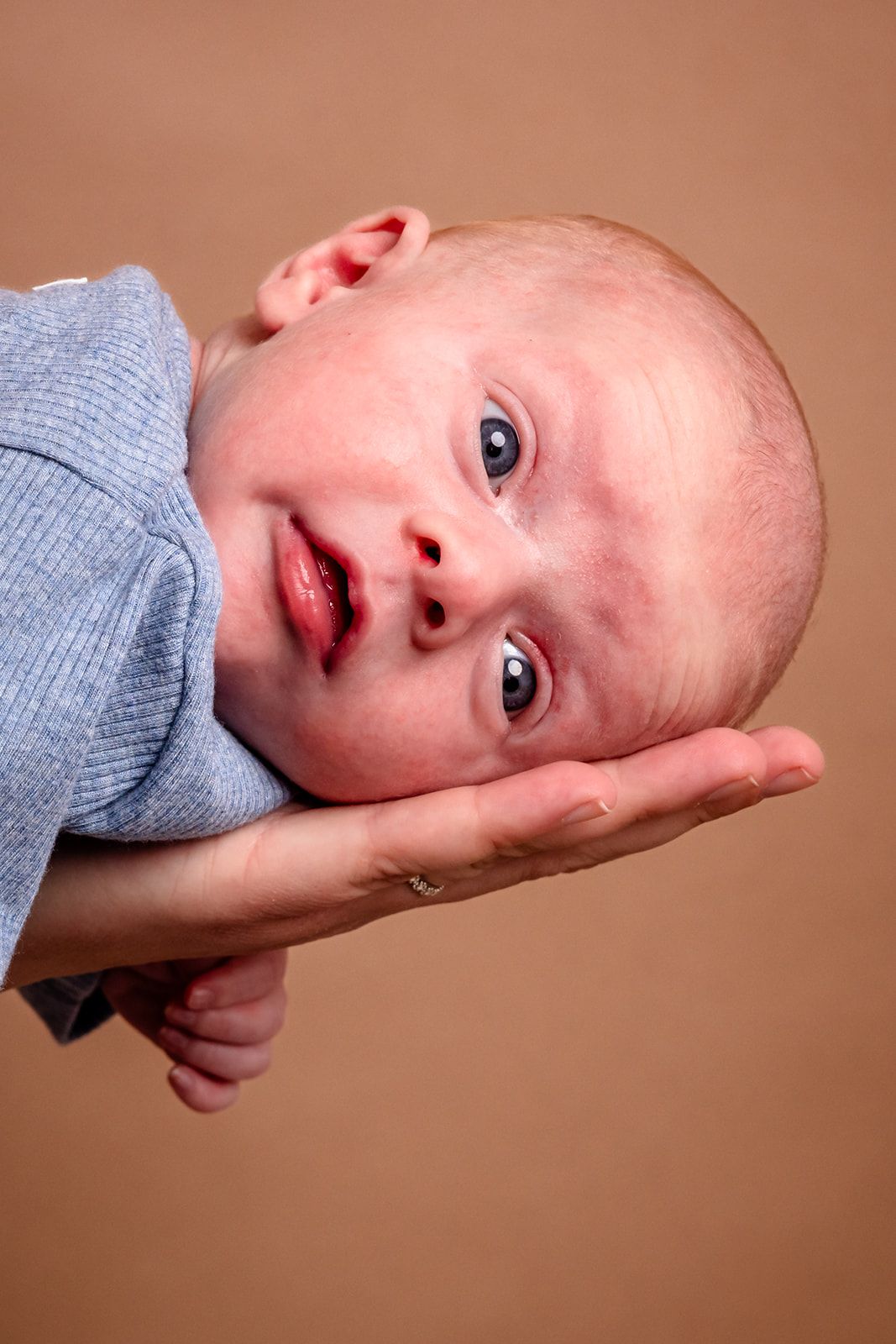 A series of close-up photos showing a baby in a blue sweater resting their head at different angles against a warm brown background.