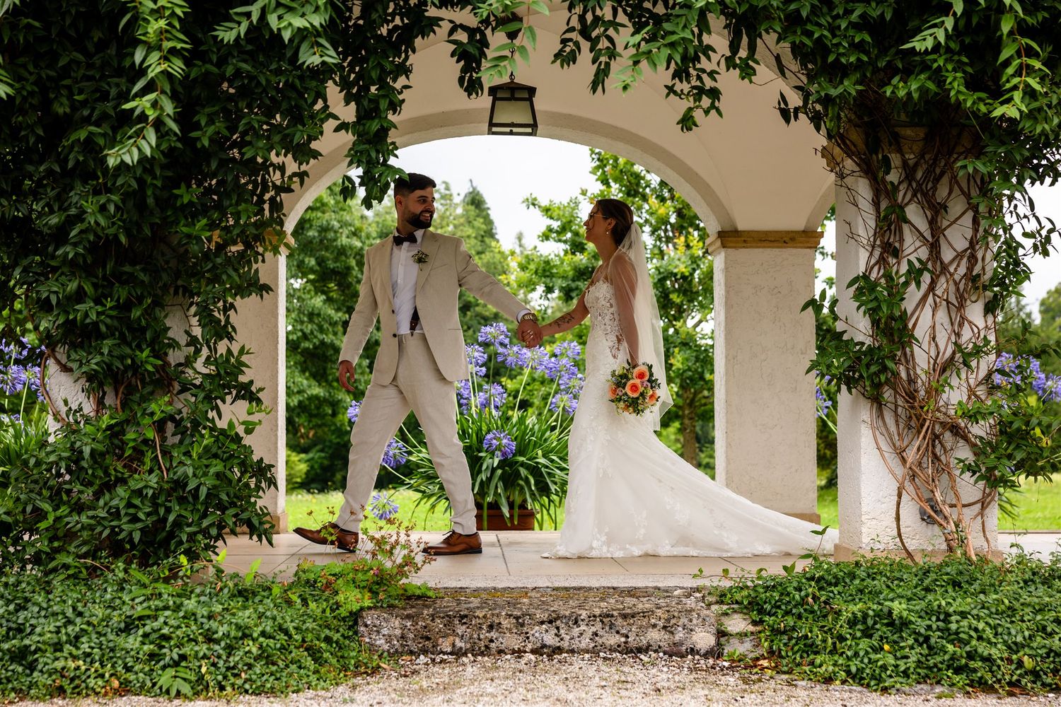 Wedding couple stands in a lush garden setting with white outfits creating a romantic atmosphere.