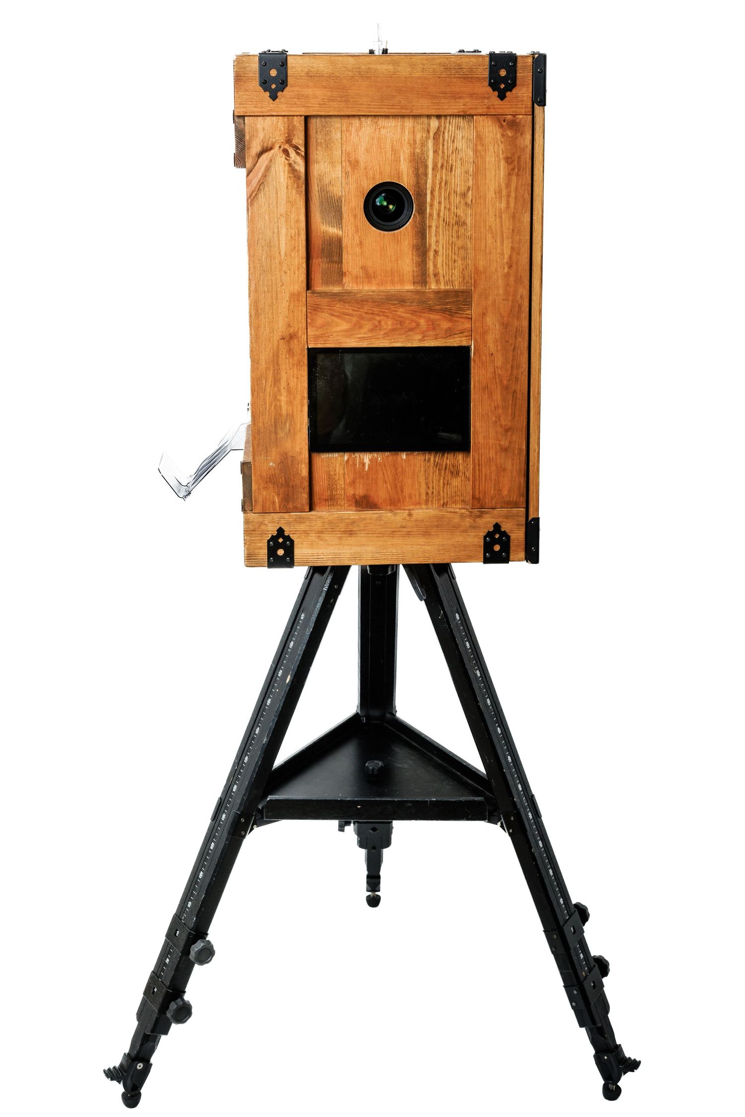 Antique wooden camera box on a black metal tripod stand, featuring brass hardware and a circular lens opening.