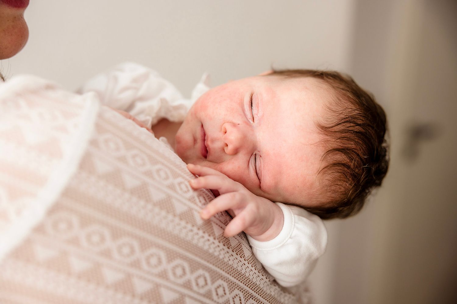 Sleeping newborn baby wrapped in delicate white lace blanket.