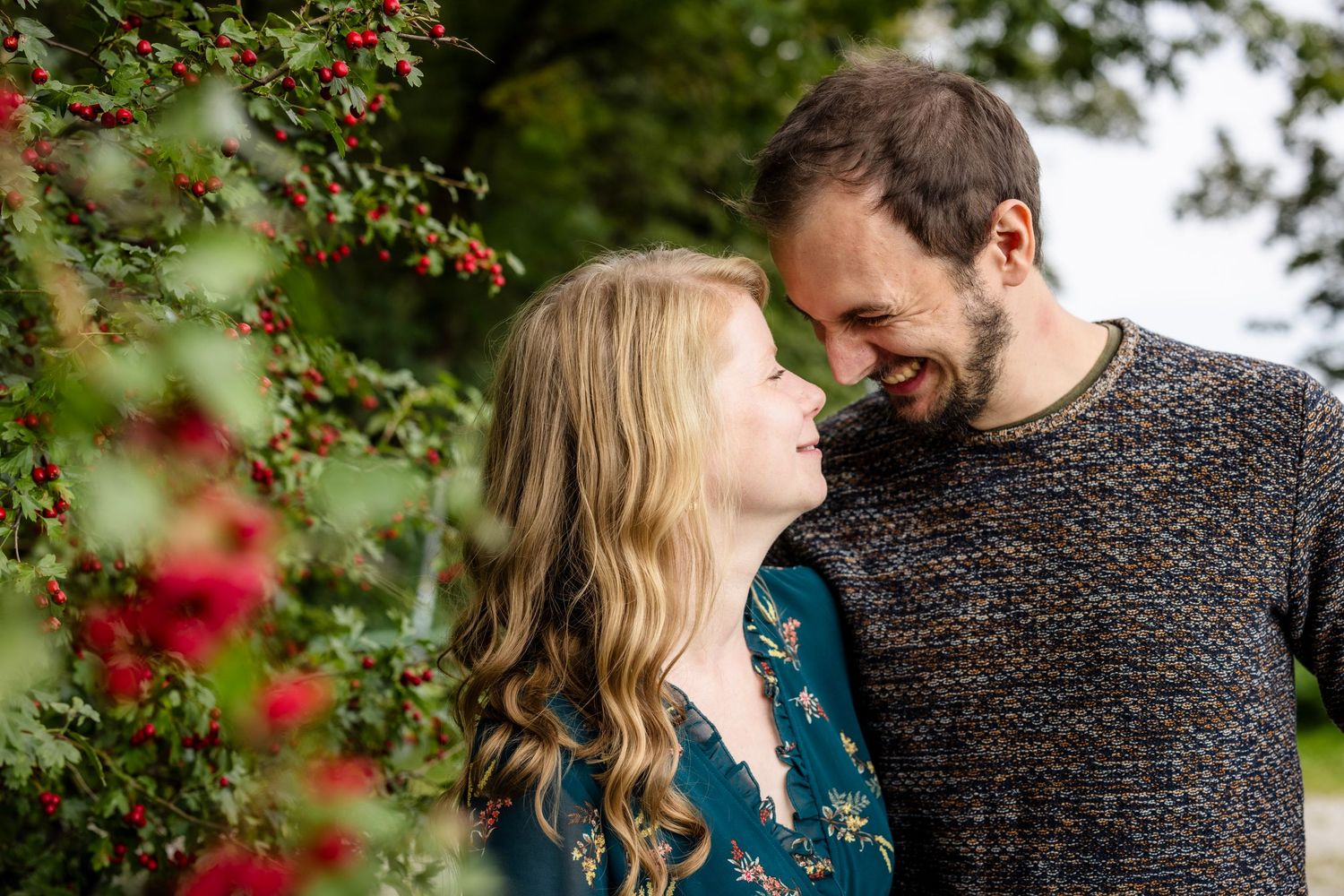 Romantic couple shares tender moments among red berries and greenery in a garden setting.