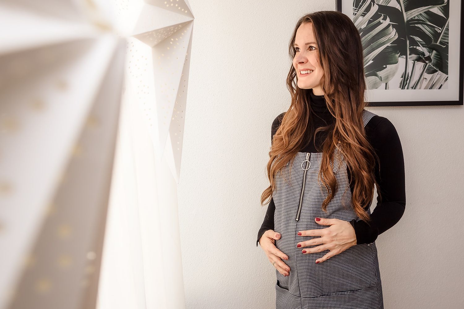 A woman in a gray sweater smiles while looking off to the side in a bright indoor setting.