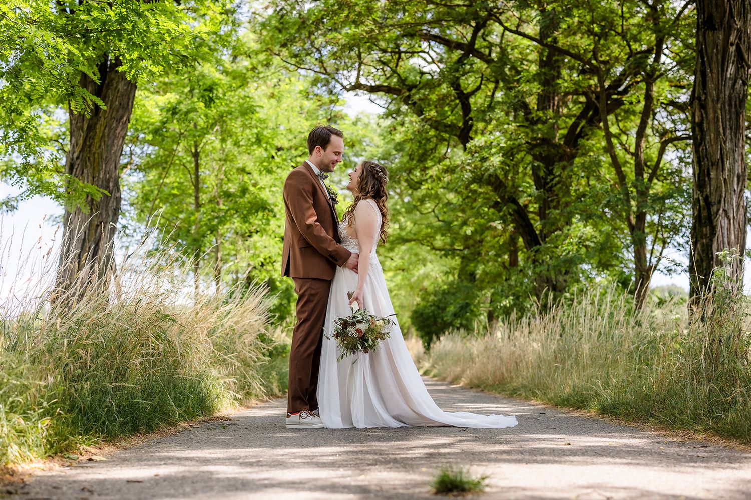 Romantic wedding photo session on a sunlit nature path with trees.