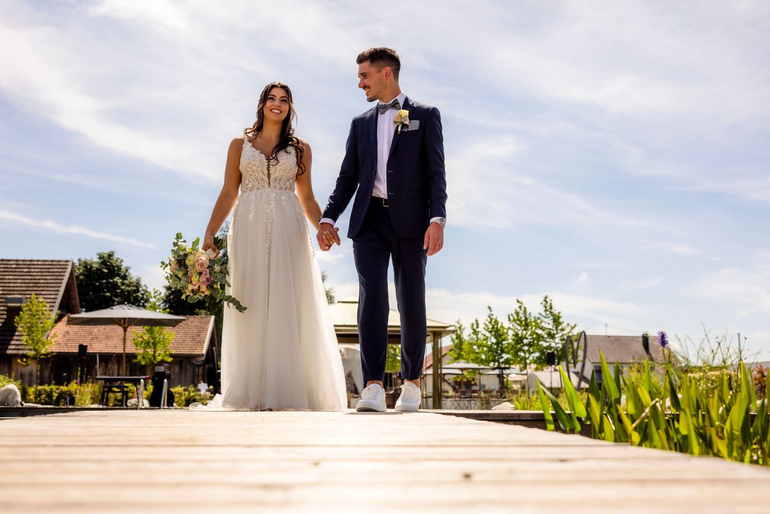 Couple walking together on a sunny day with lush greenery and scenic views in the background.