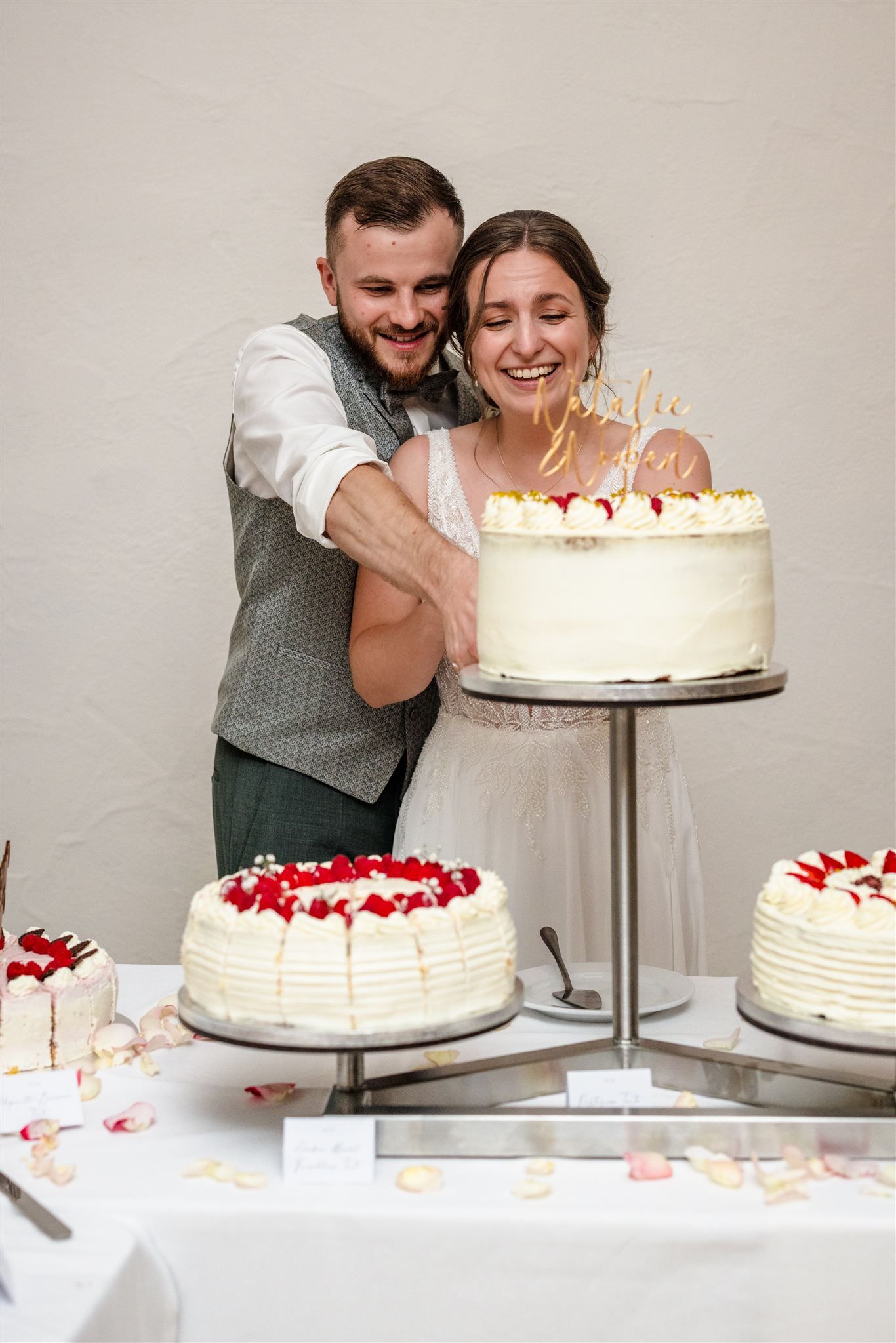A sequence of photos showing a couple cutting into a white tiered wedding cake decorated with red berries and cream.