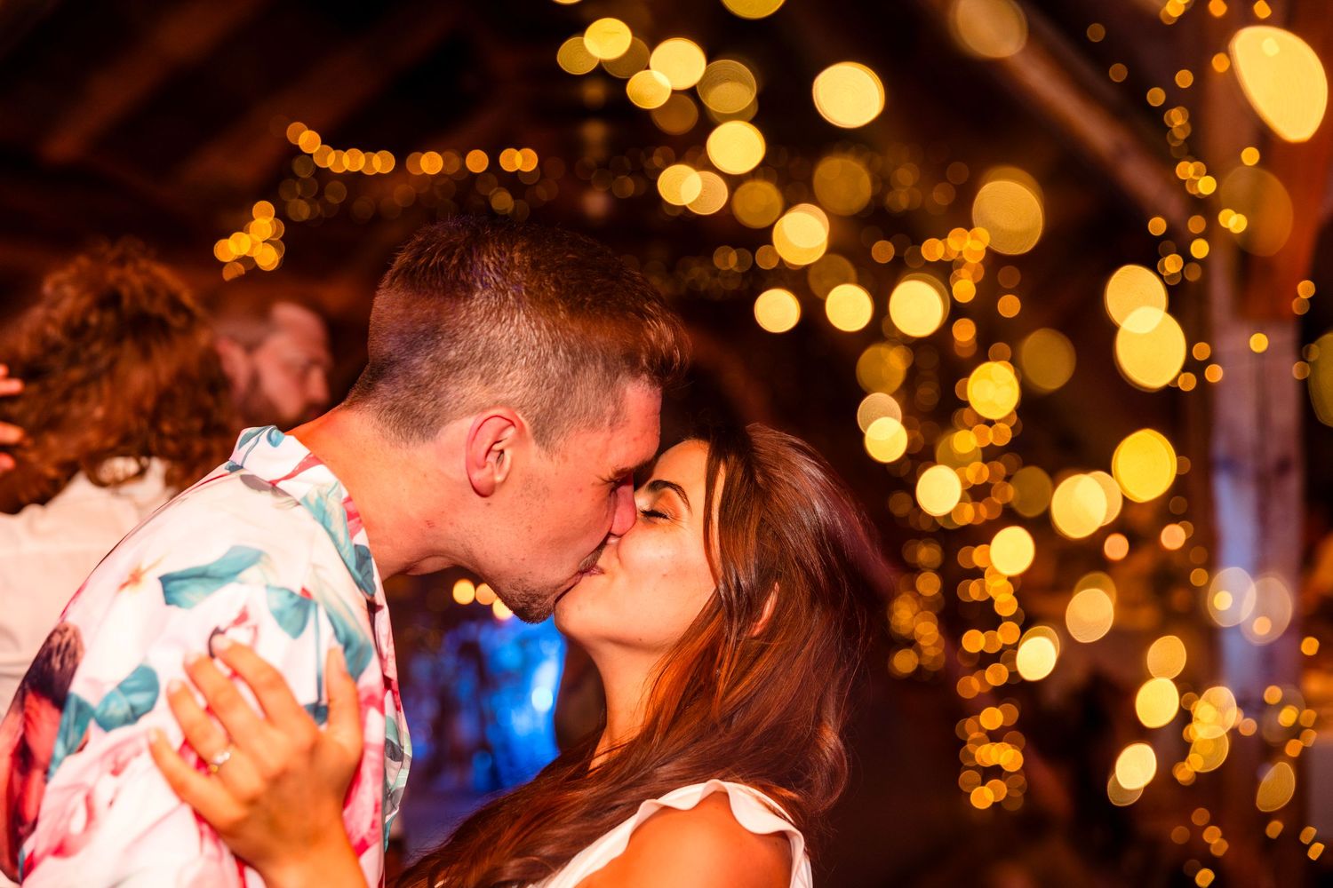 A romantic couple shares a kiss at night with glowing golden bokeh lights creating a magical atmosphere in the background.