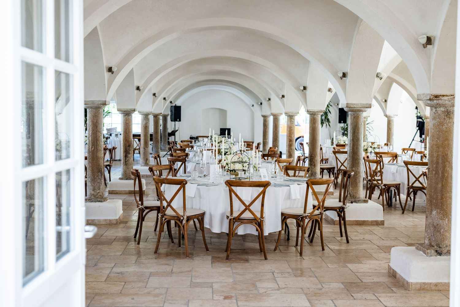 Bright white arched hallway with wooden chairs and tables set up for dining in an elegant restaurant setting. Hofgut Sickertshofen