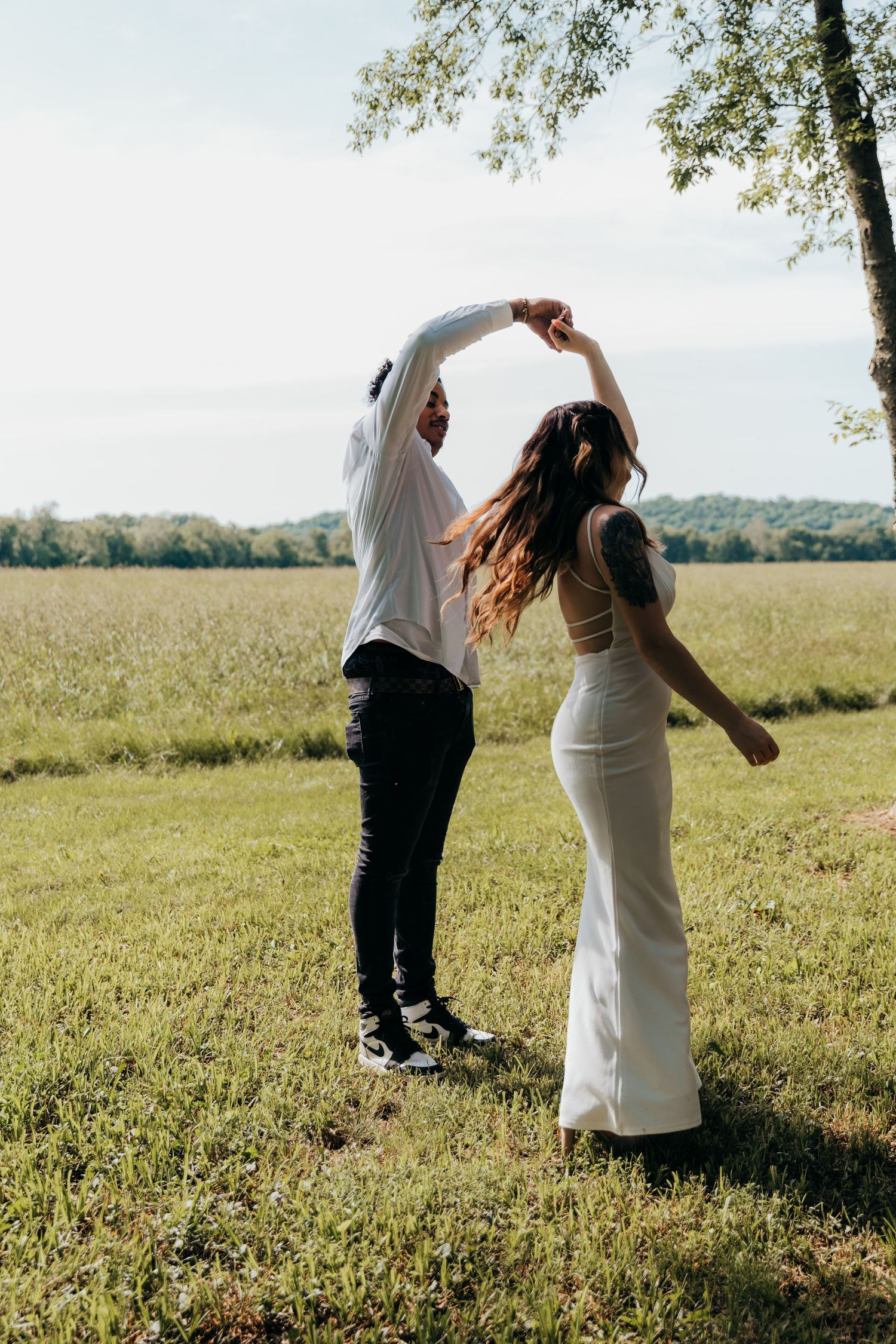 Couple dancing in a sunlit meadow with rolling hills in the background.