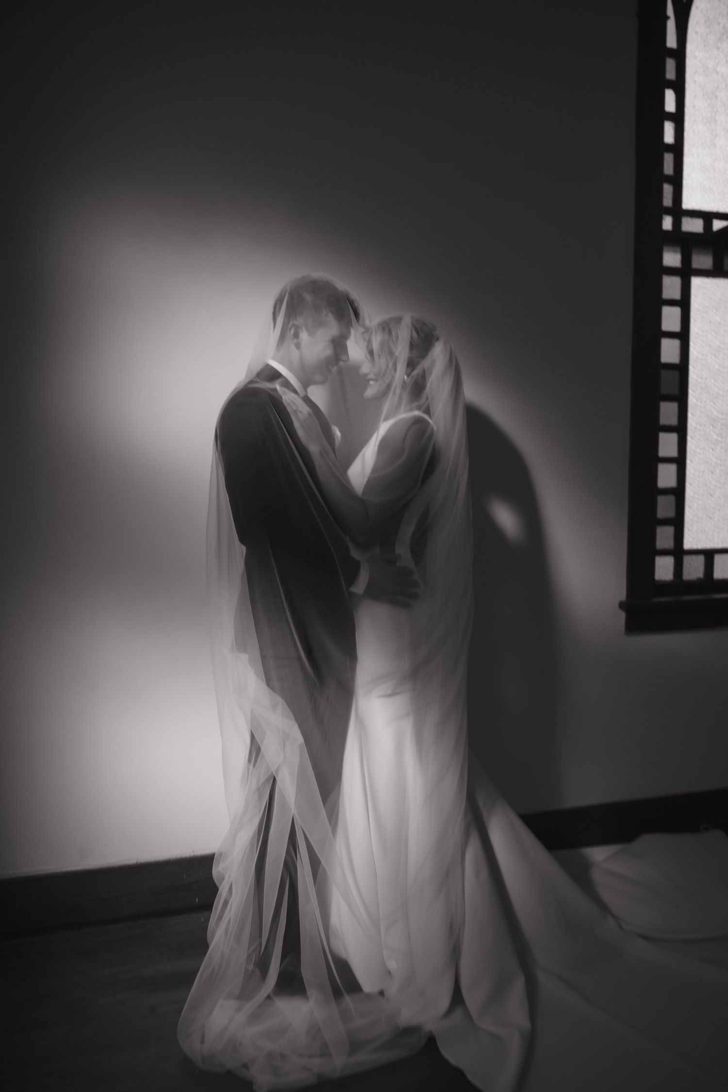 Artistic black and white wedding portrait with dramatic shadows and lighting.