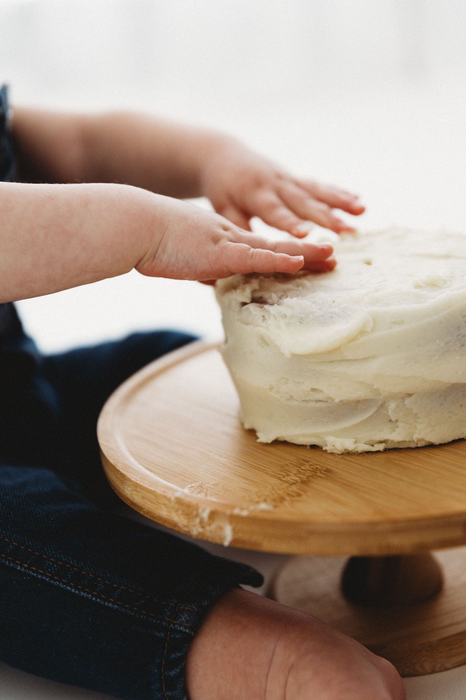 Hands shaping and smoothing white frosting on a wooden cake board in a step-by-step sequence.
