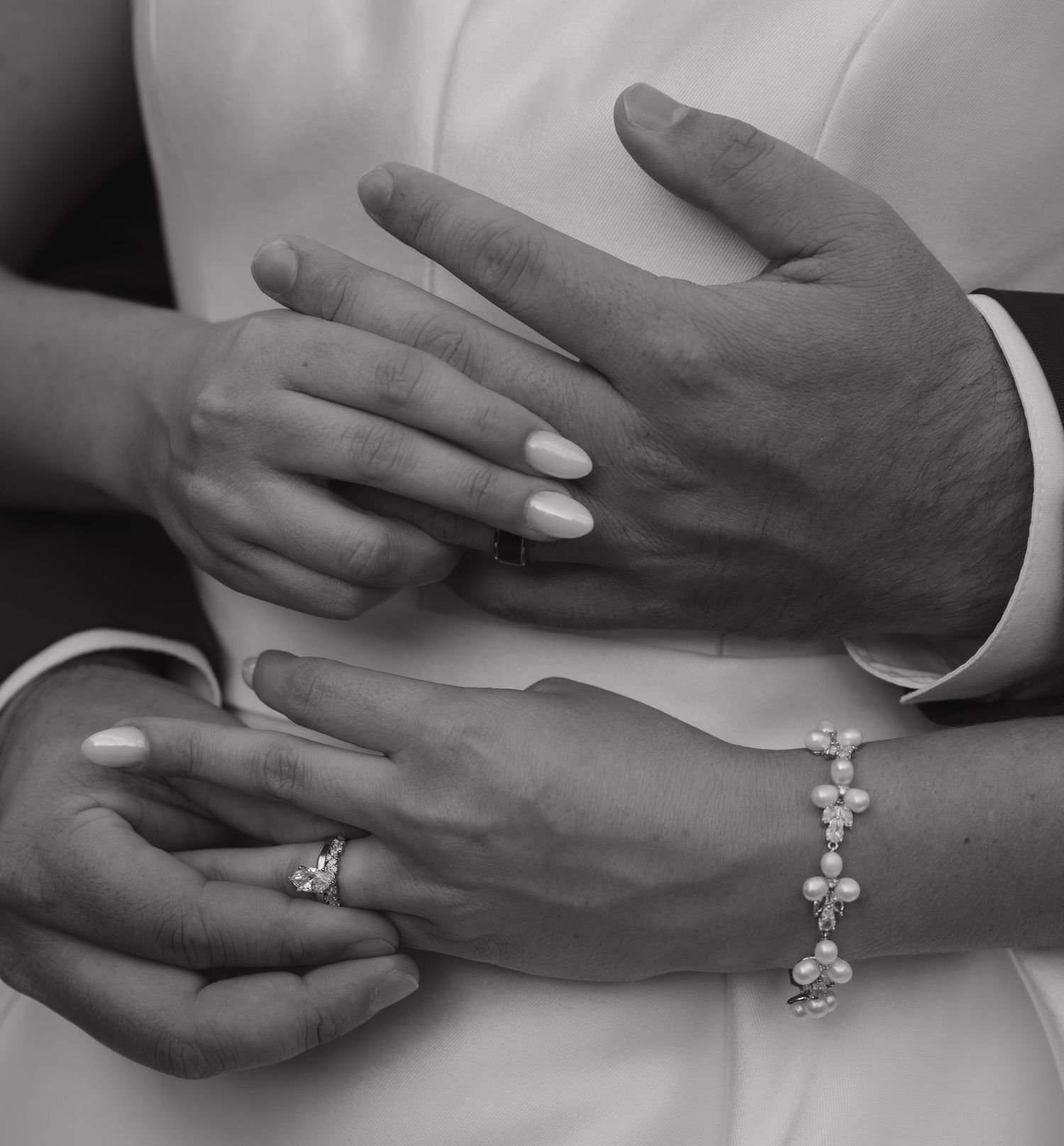 Black and white close-up of hands wearing wedding rings, with one person wearing an elegant crystal bracelet.