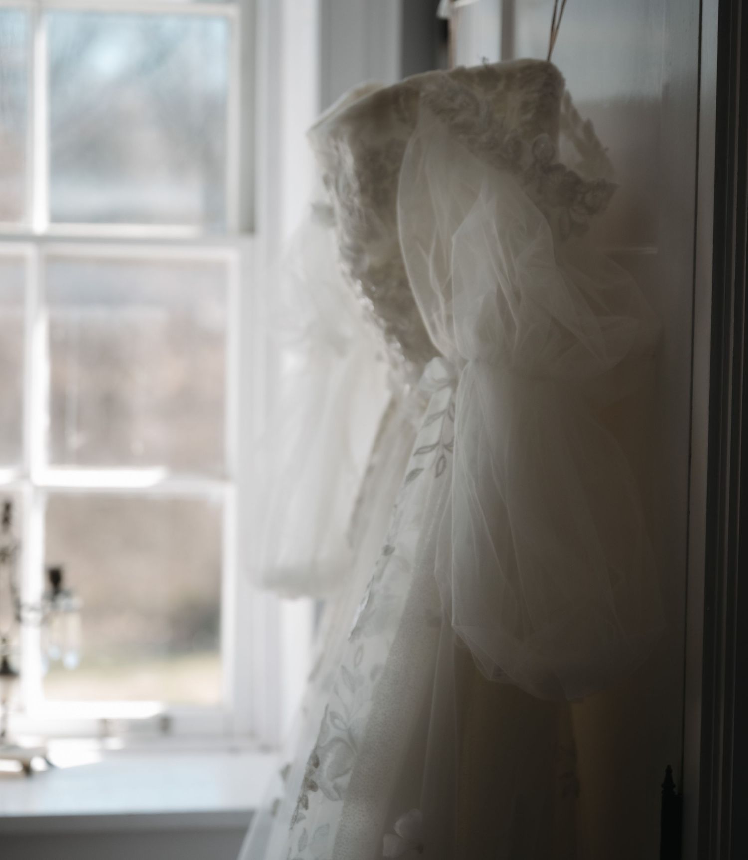 White wedding dresses hanging in a row near bright windows creating a soft, ethereal display.