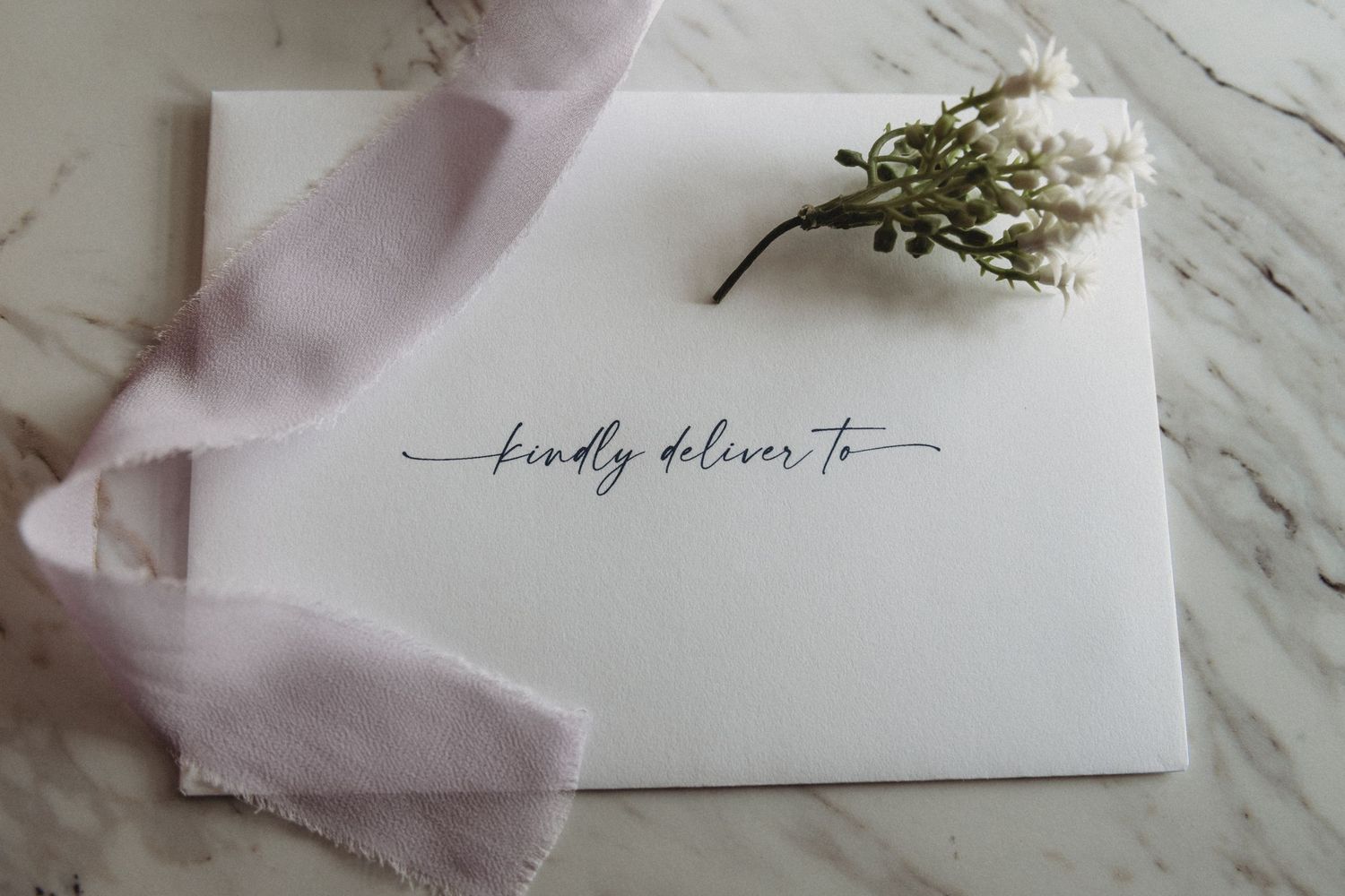 Elegant white silk ribbon and calligraphy wedding stationery styled on white marble surface.