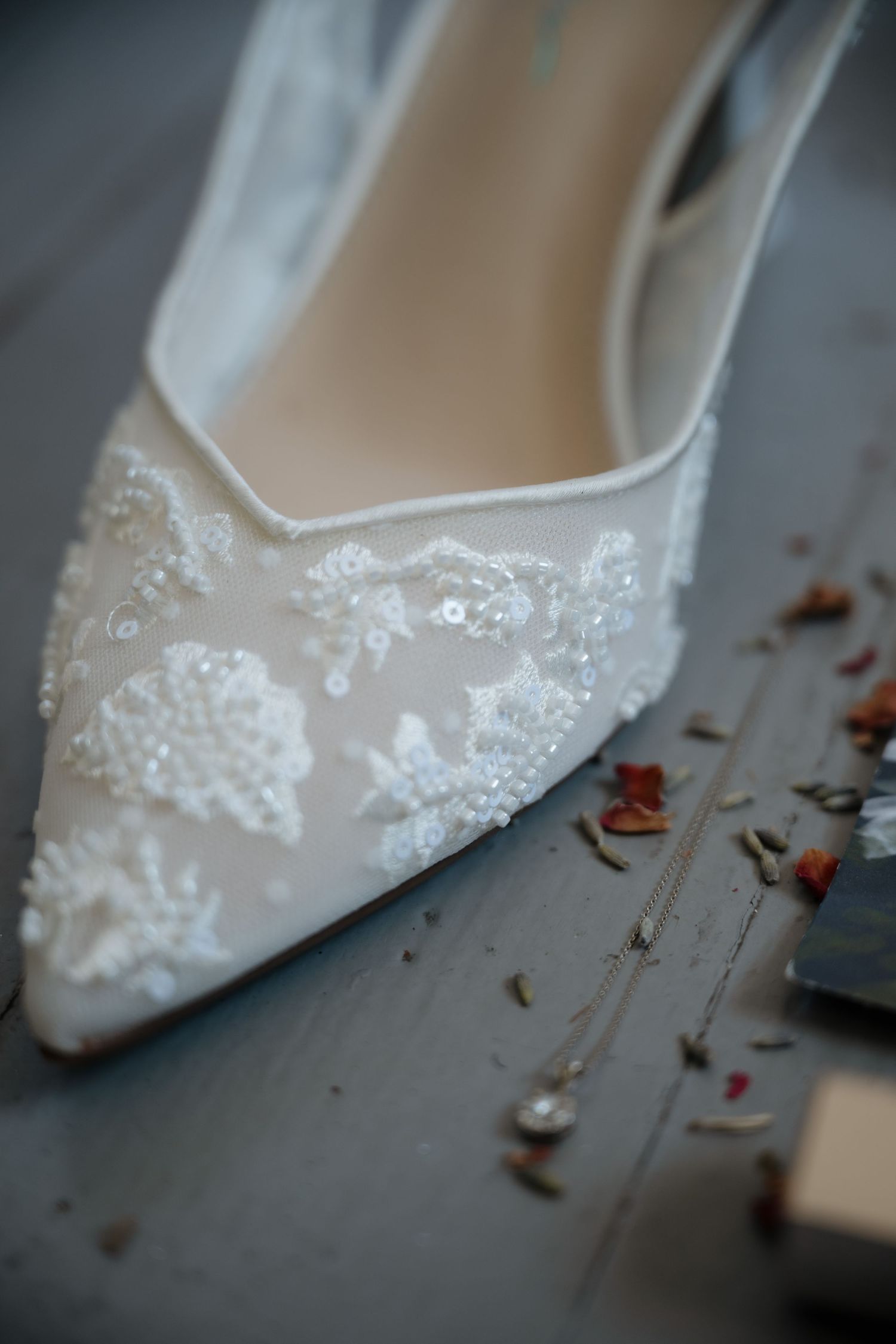 Elegant white bridal shoe with delicate lace and sequin embellishments shown in close-up detail.