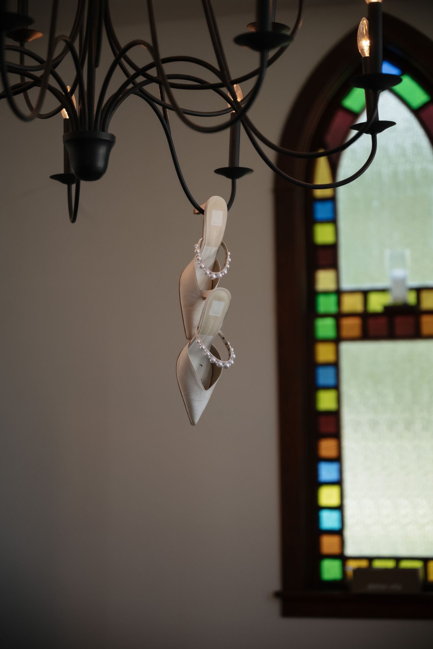 Hanging light fixtures against stained glass window in church interior.