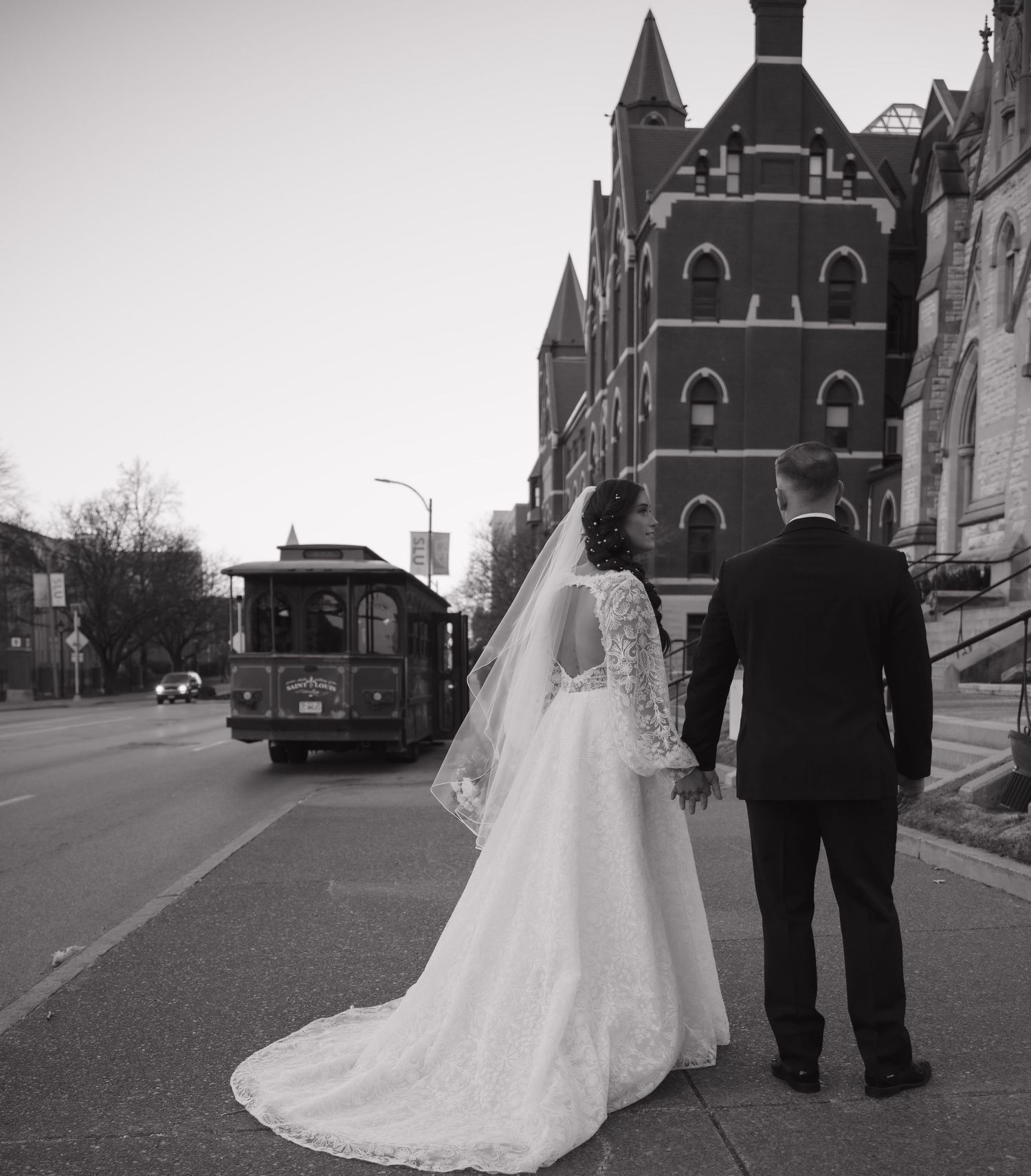Black and white photo of a couple in wedding attire walking down a historic brick street.