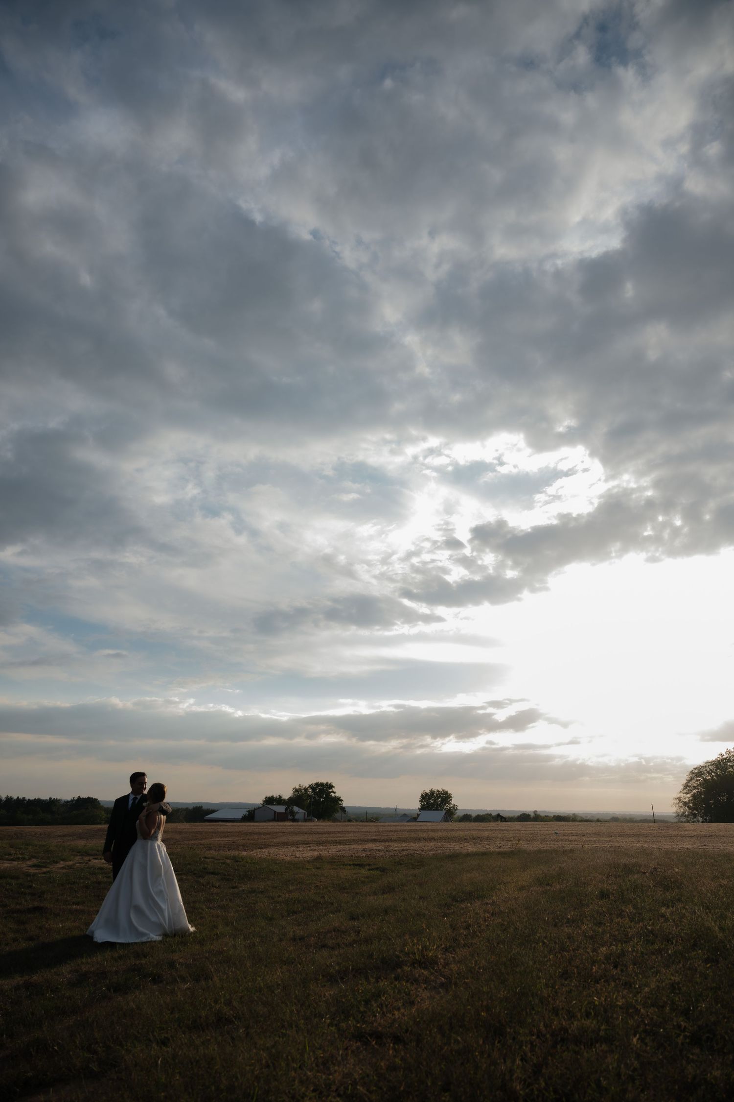 Dramatic wedding silhouette against a moody sunset sky over an open field.