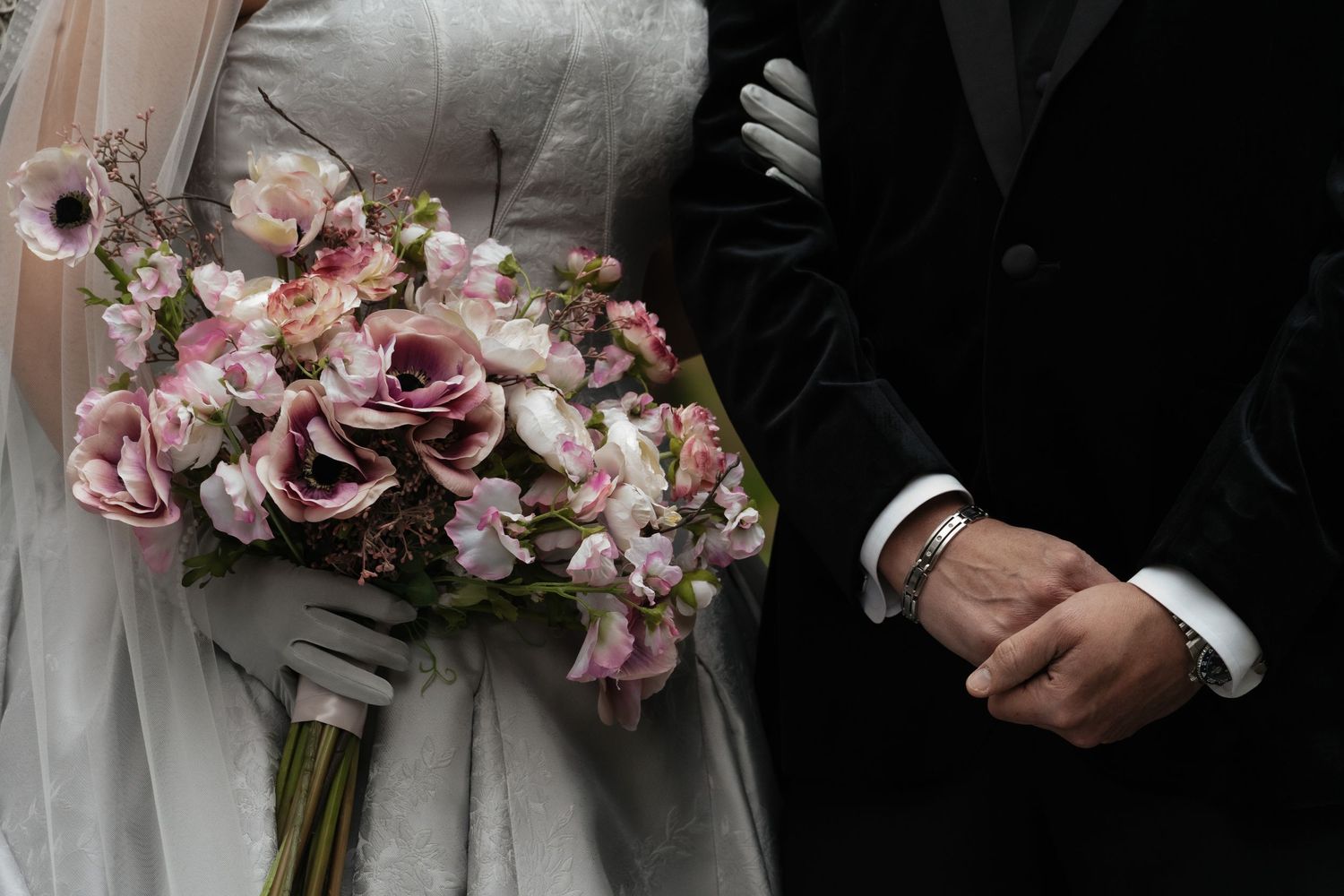 A bride and groom hold hands while their wedding party carries pink and white floral bouquets.