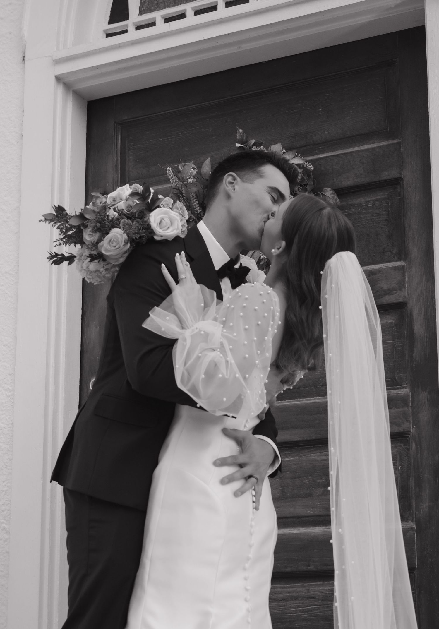 Black and white wedding portrait captured in front of a classic white doorway.