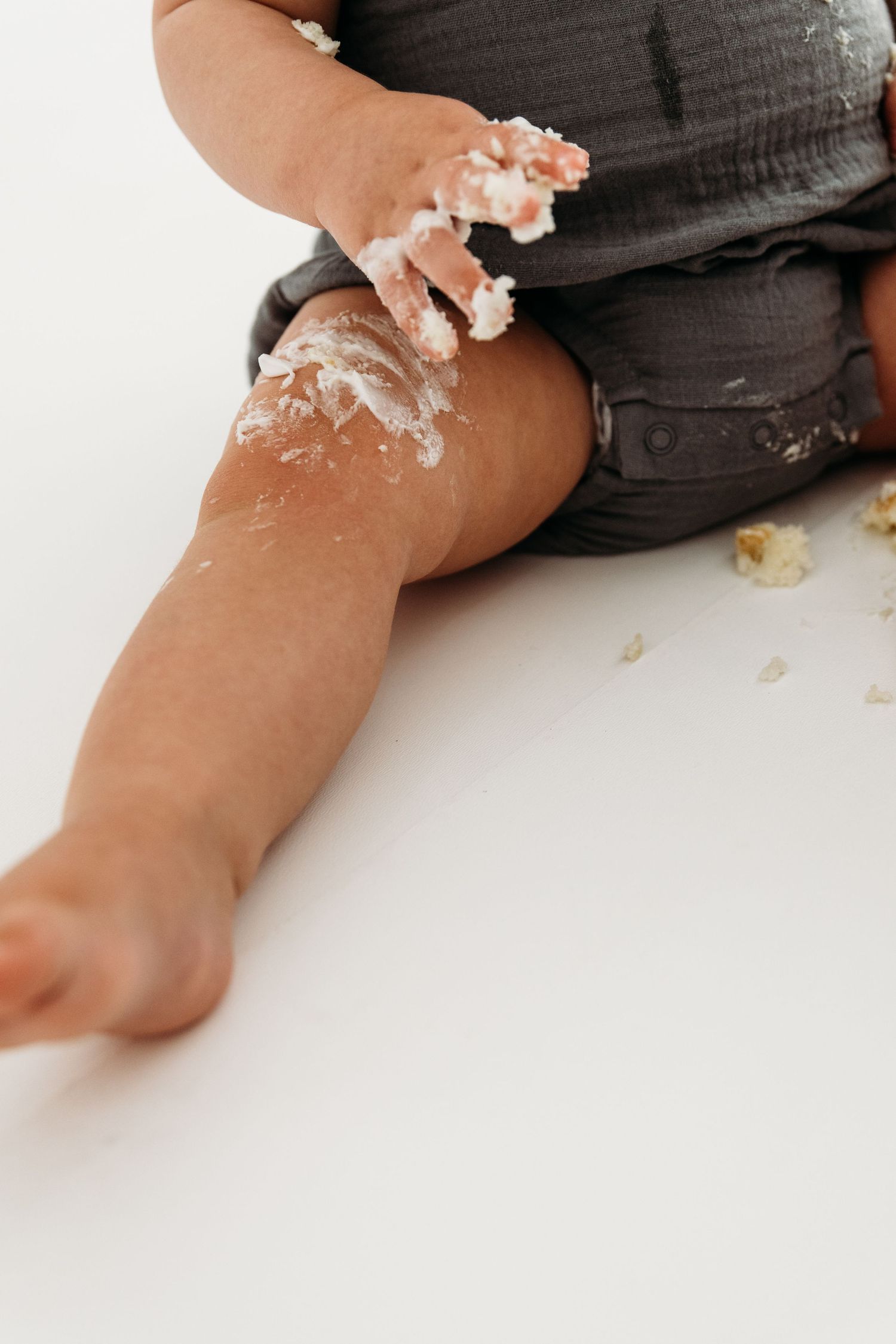 Small baby hands covered in white frosting and cake crumbs against a clean white background.