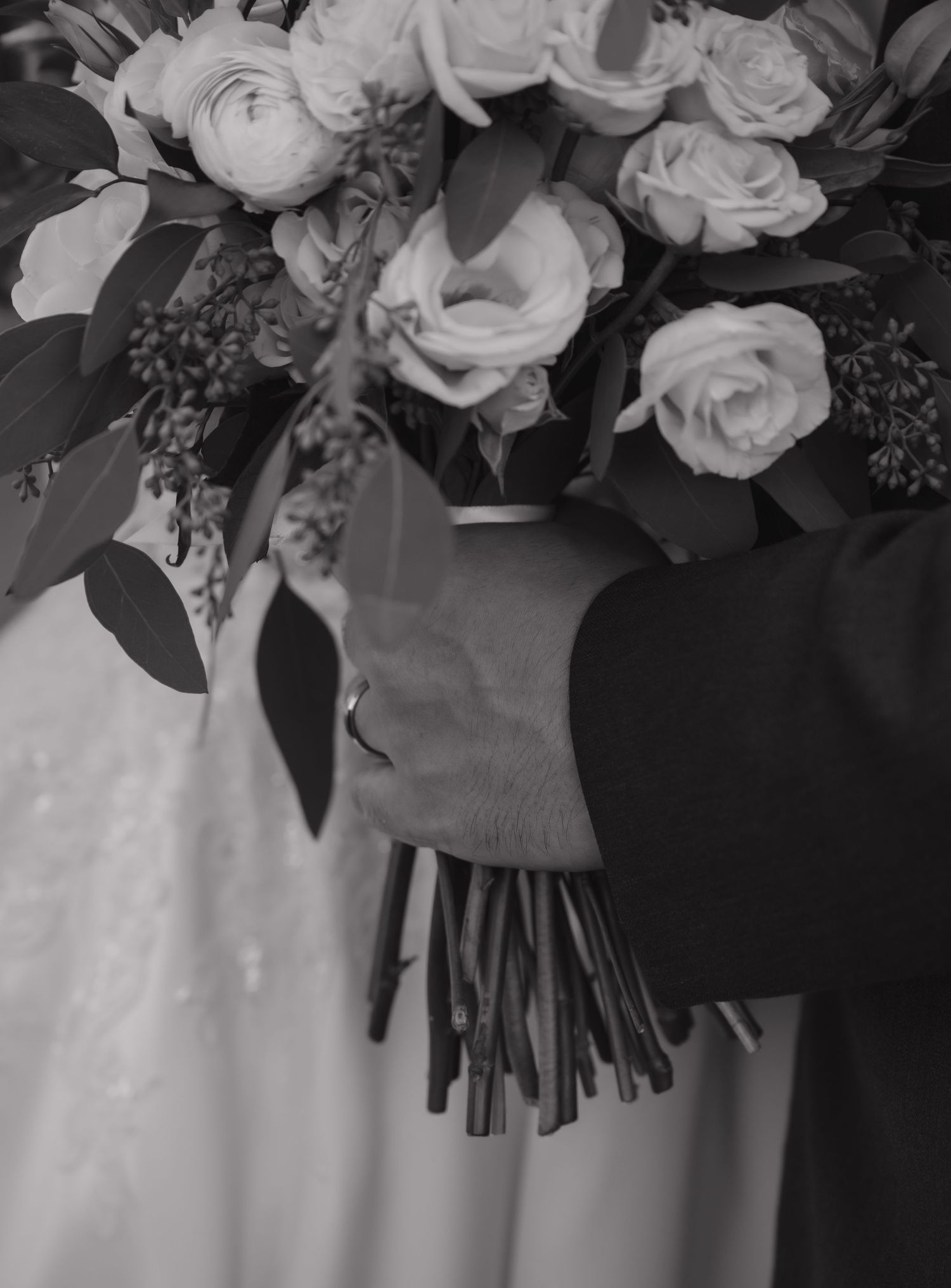 Close-up of white rose wedding bouquet against bridal gown.