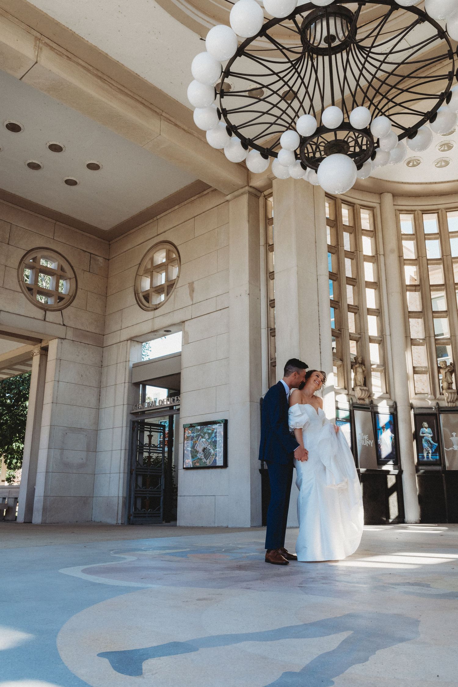 A wedding couple poses in an elegant indoor rotunda with ornate architectural details and white columns.