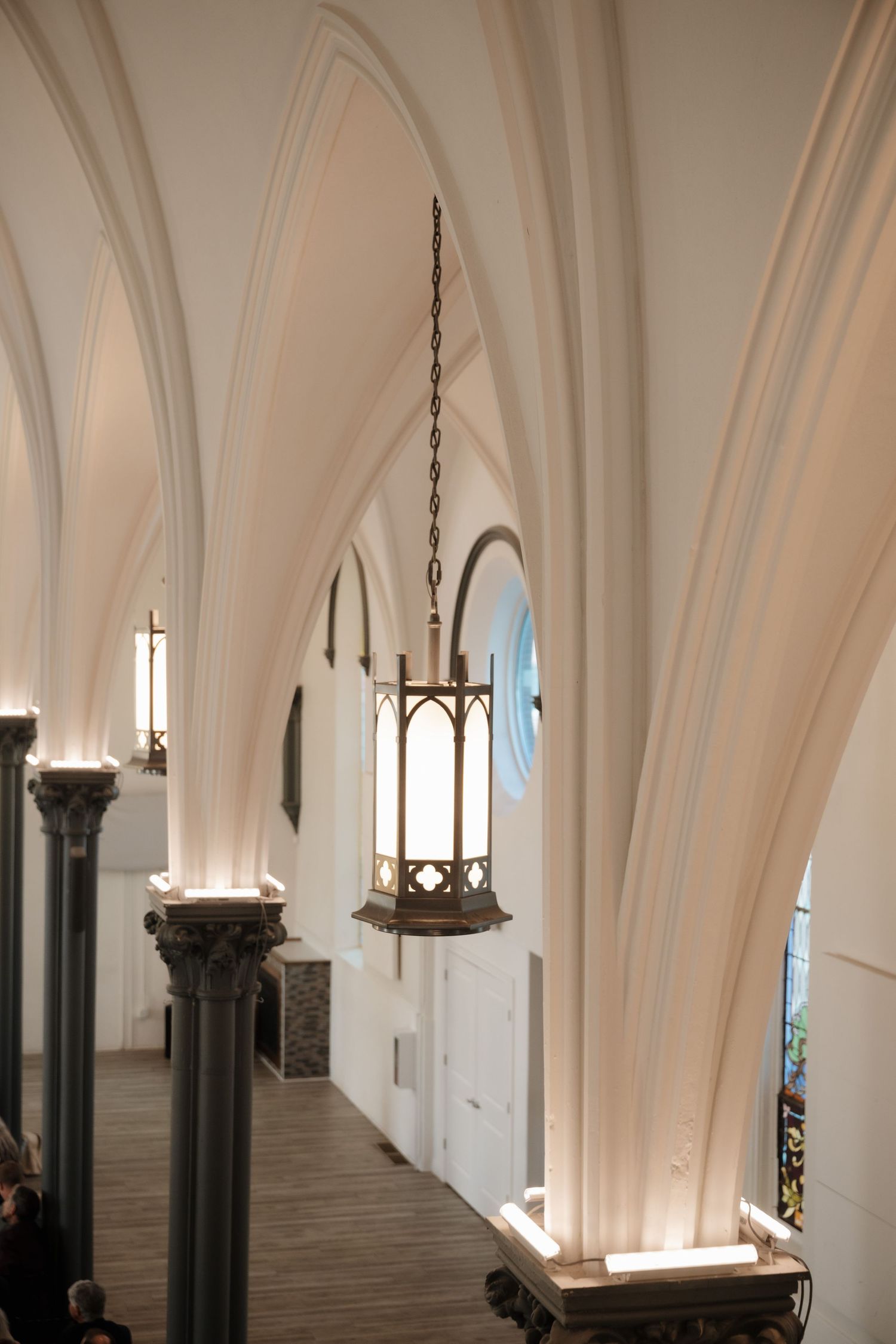 Gothic church interior hallway with vaulted ceiling and hanging pendant lights.