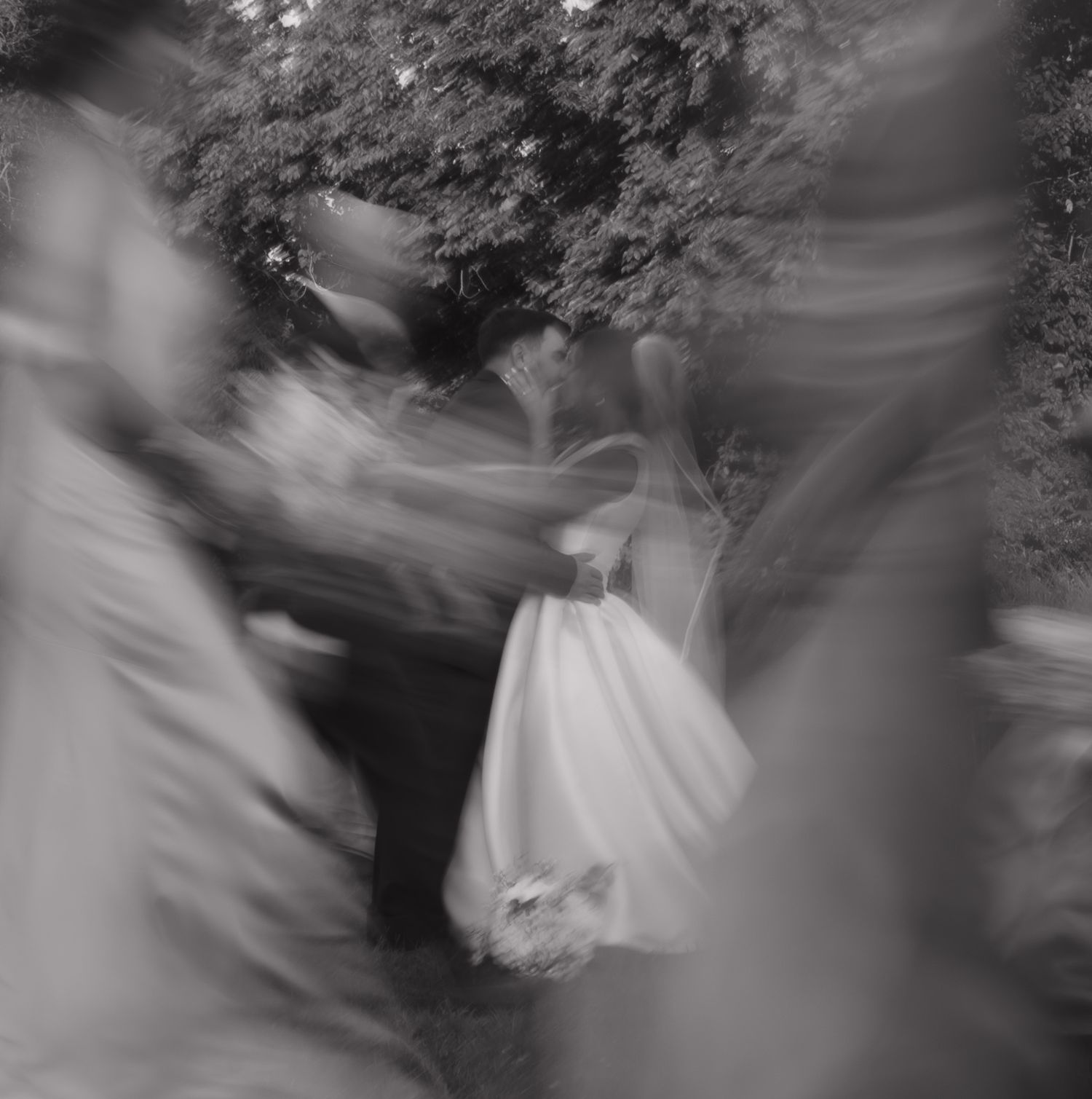 Ethereal black and white motion blur photograph of figures dancing at an outdoor wedding celebration.