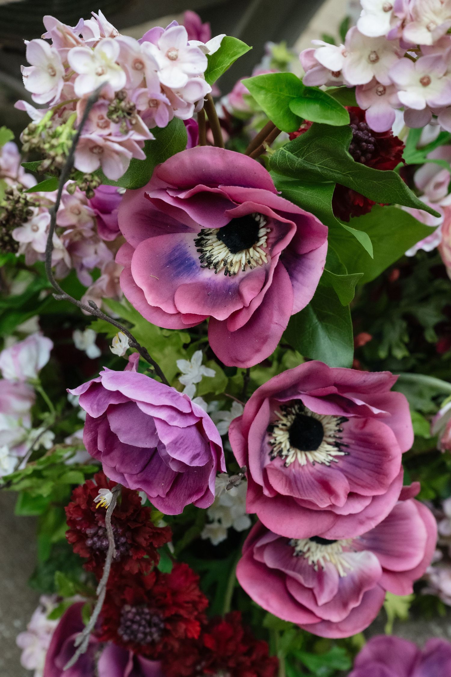 Beautiful purple anemone flowers with dark centers mixed with pink hydrangeas and greenery in a floral arrangement.