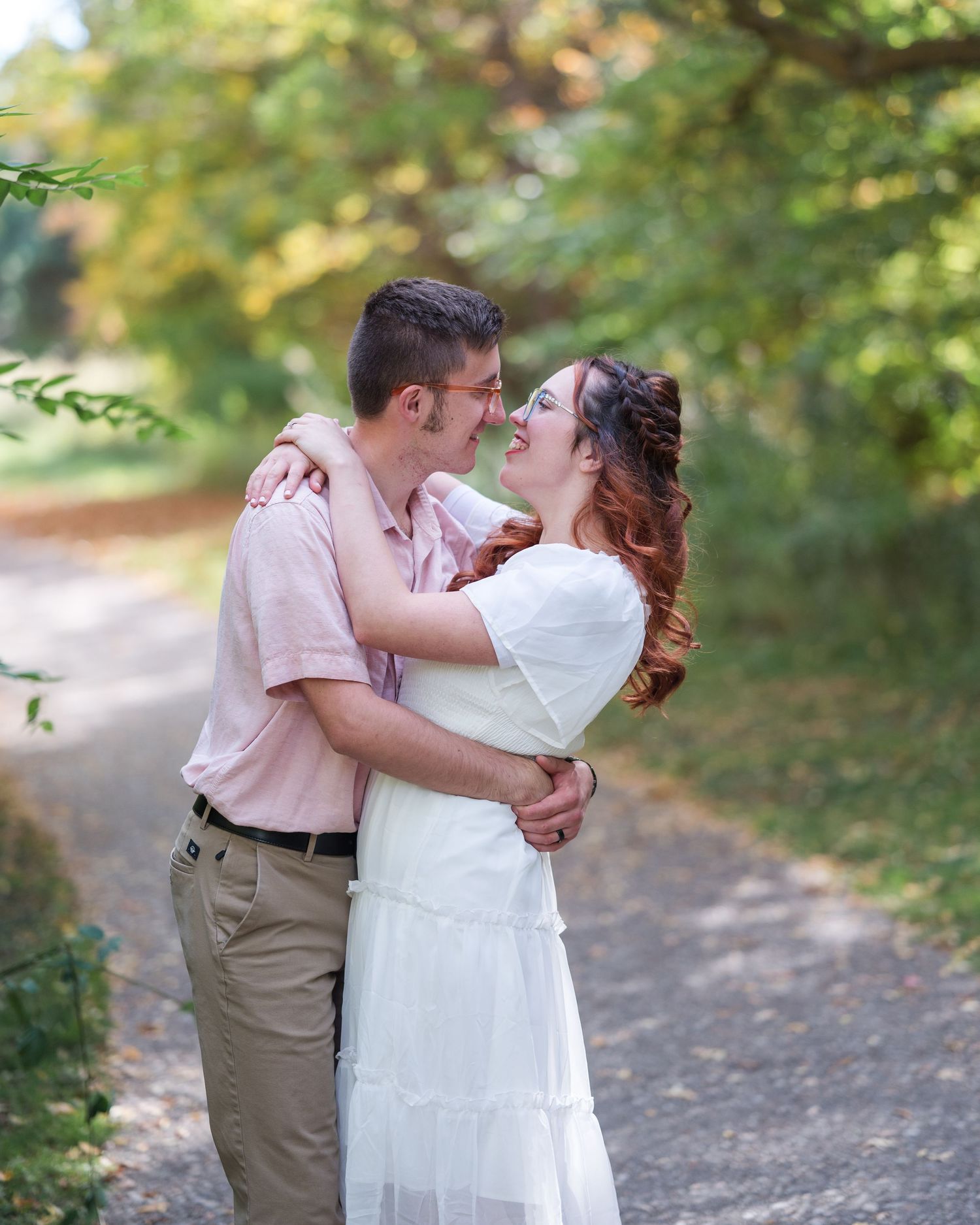 A romantic couple embraces on a wooded path during an outdoor photo session in natural lighting.