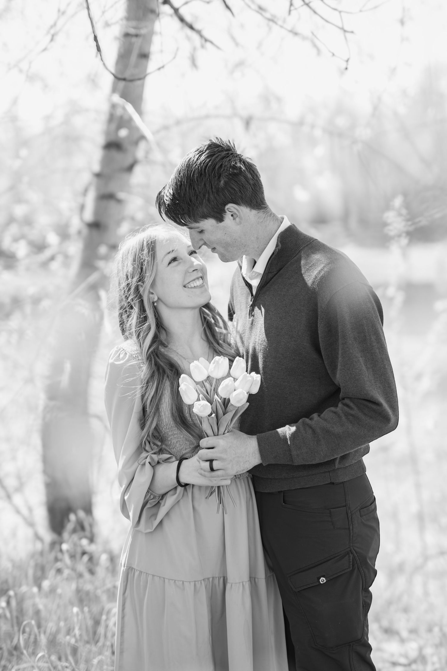 Black and white photo of a couple sharing a romantic moment outdoors, woman holding tulips and smiling.