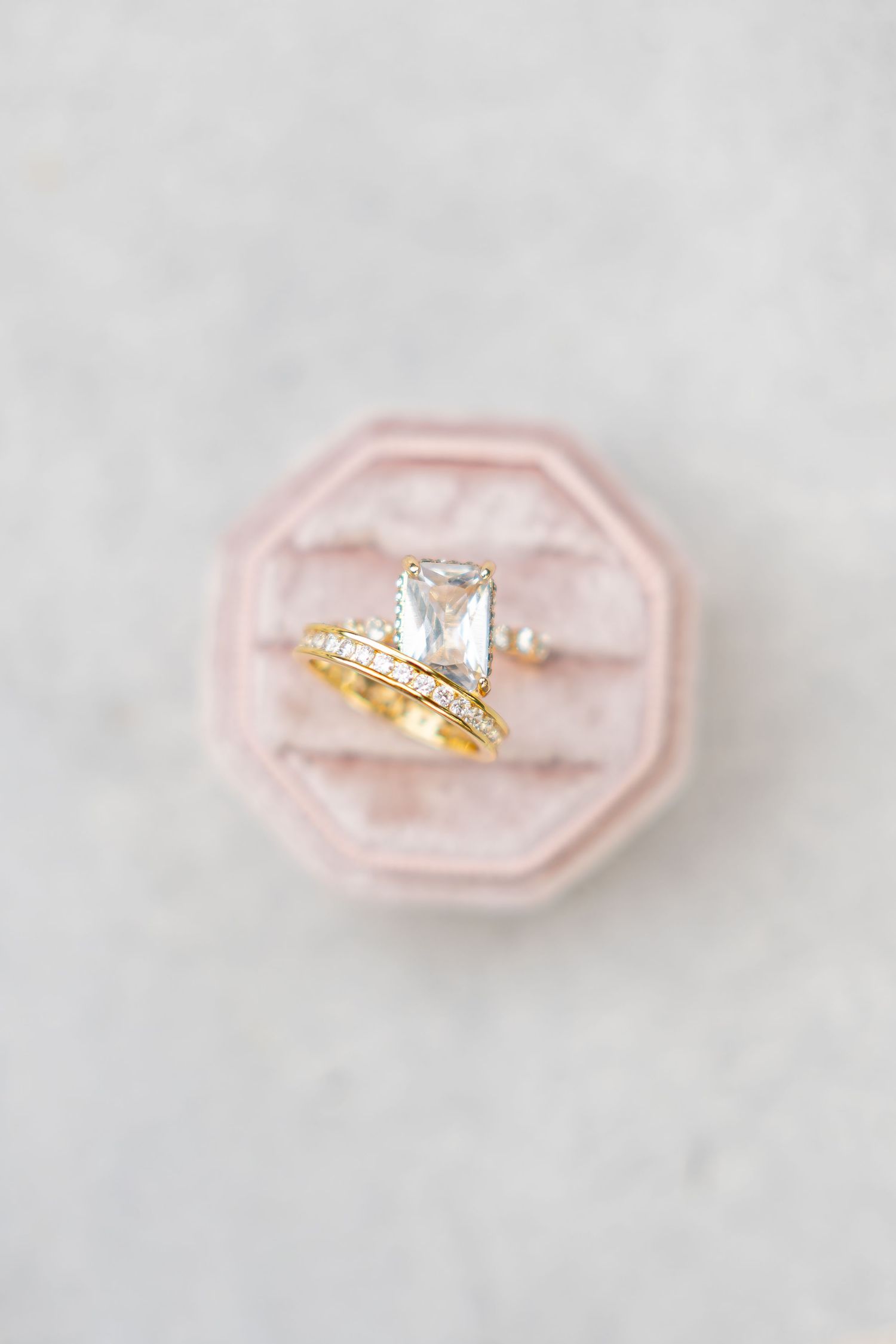 Gold engagement ring set with baguette diamond solitaire and pavé band displayed in pink velvet octagon ring box.