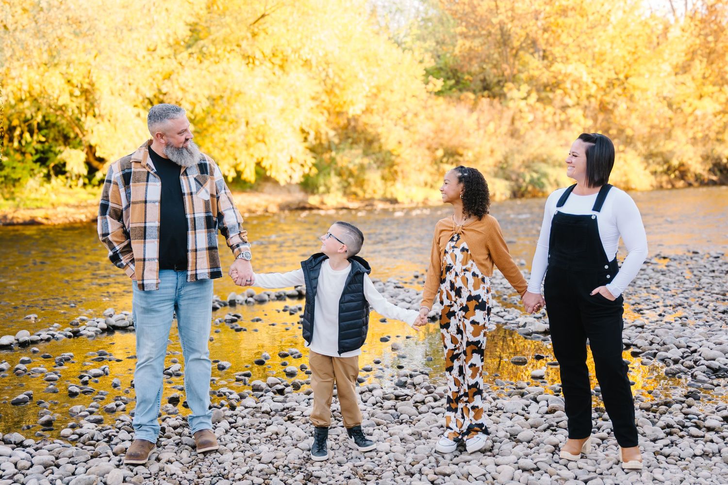 Family walking together on a rocky riverbank during golden autumn sunset with trees in background.