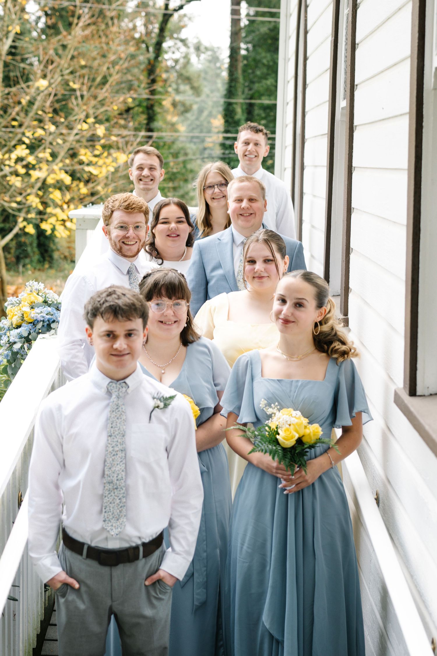 Wedding party poses together on a covered bridge wearing dusty blue bridesmaid dresses and gray suits.