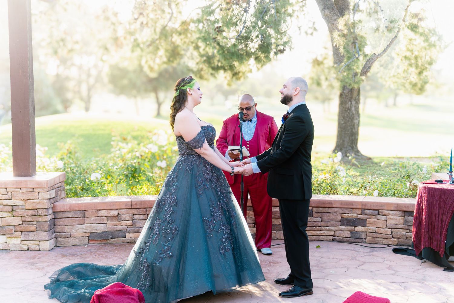 Bride in blue gown and groom in white suit exchange vows outdoors at a rustic stone wedding ceremony.