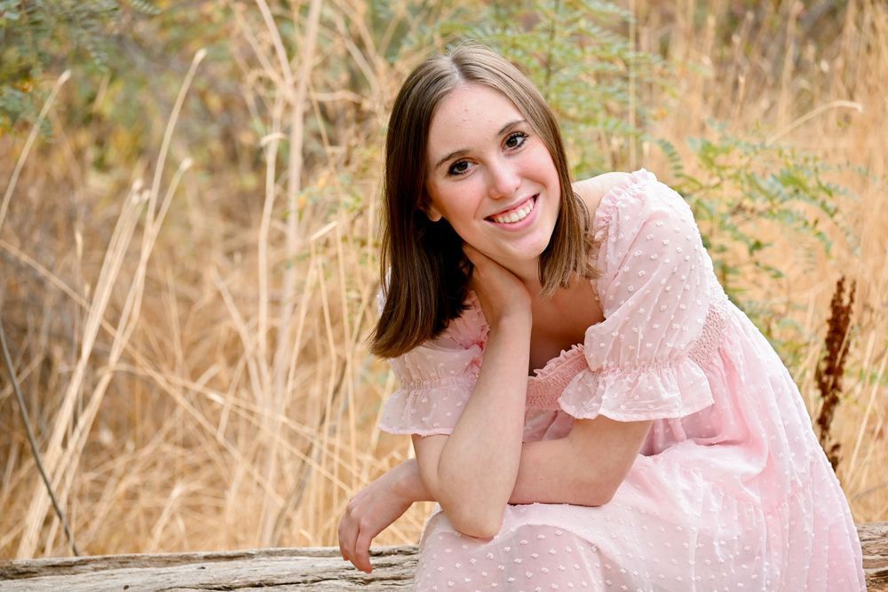 Someone in a soft pink dress poses outdoors in a natural setting with golden grass and sunlight.
