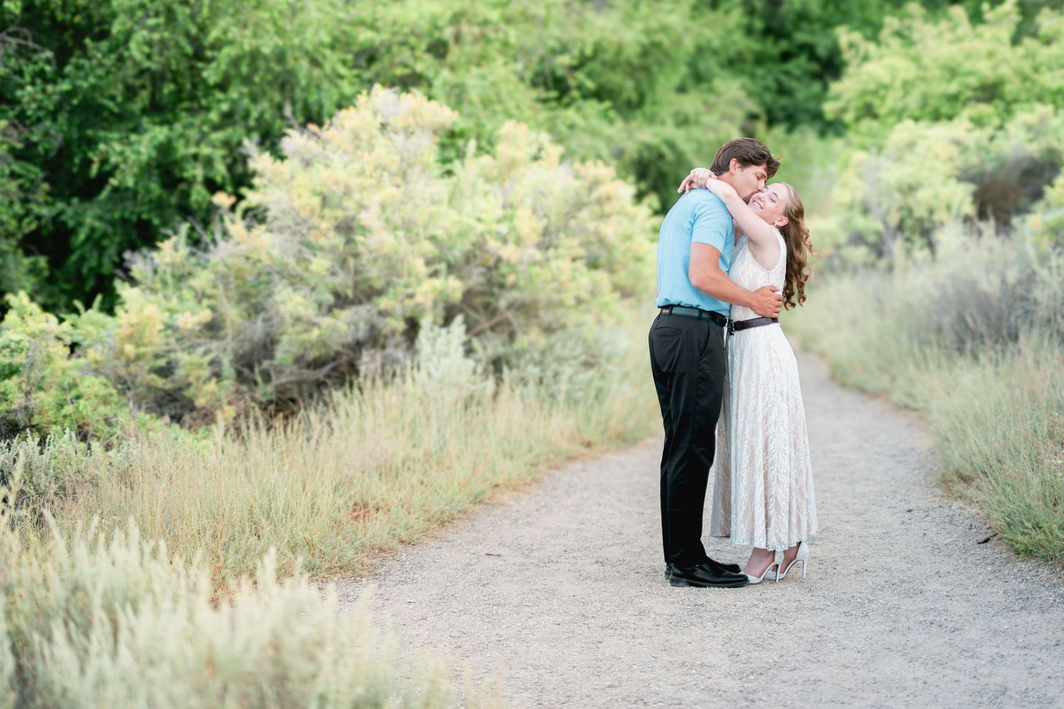Couple embracing and kissing on a scenic garden path surrounded by lush green shrubs and wildflowers.