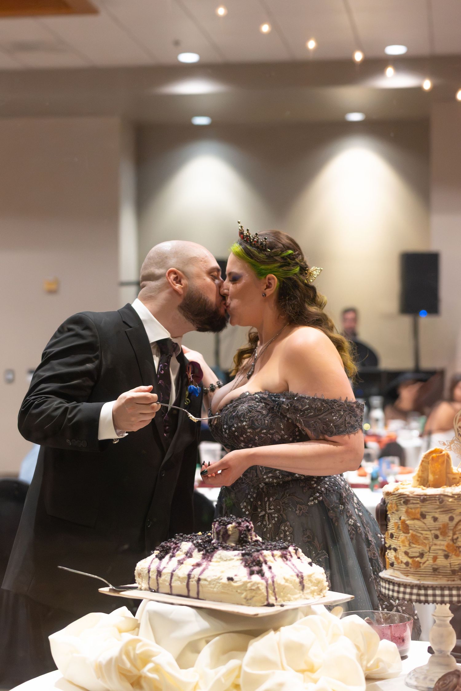 Bride and groom sharing a kiss while cutting their wedding cake at a elegant indoor reception venue.