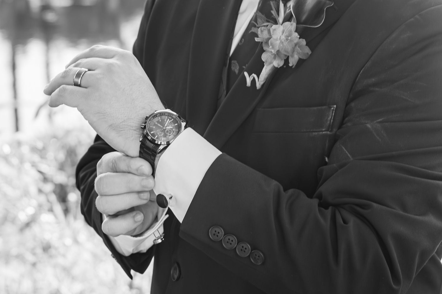 Black and white photo of a groom adjusting his luxury watch, wearing a suit with boutonniere on his wedding day.