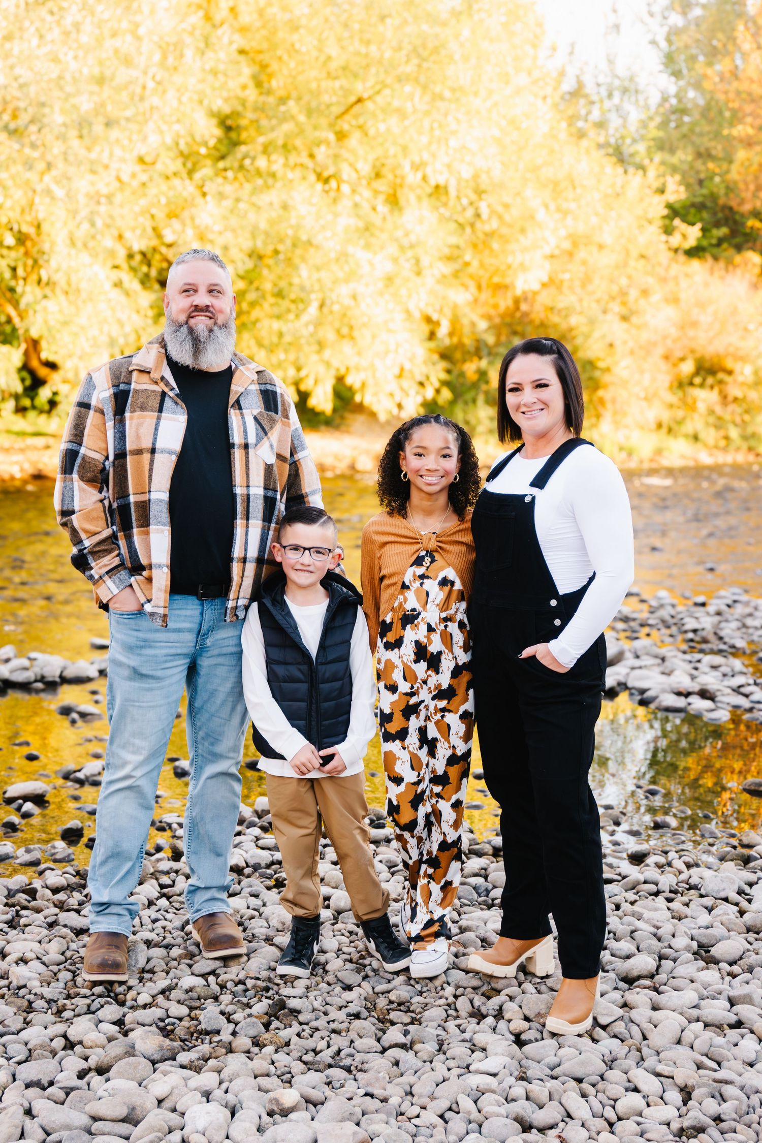 Family photo sequence on rocky riverbank with autumn foliage in background.