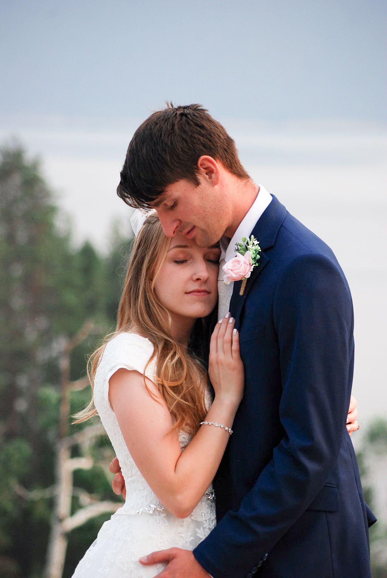 A romantic wedding moment captured outdoors with a couple embracing, the bride in white and groom in navy blue.