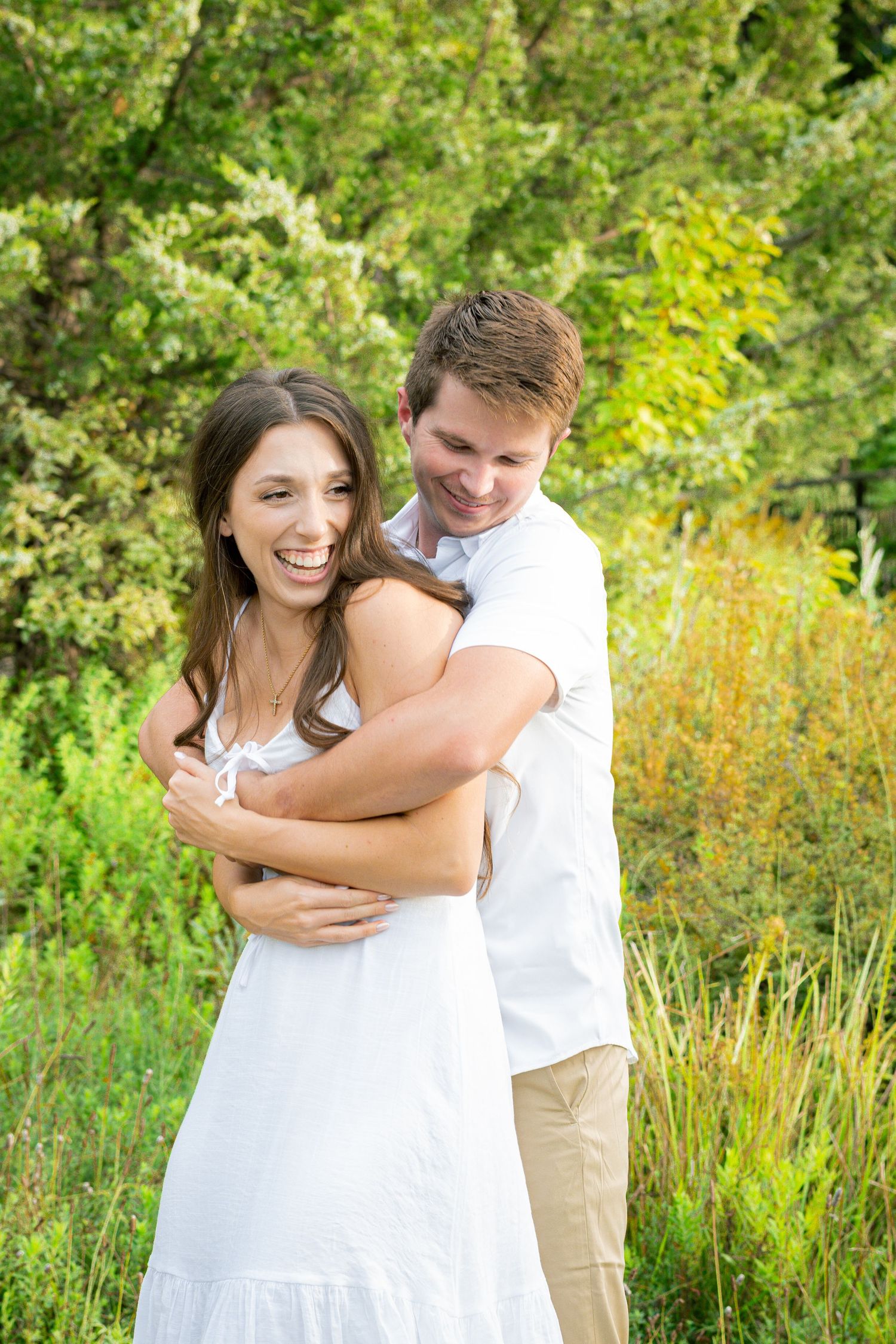 Joyful couple embracing and laughing in a sunny meadow with wildflowers.